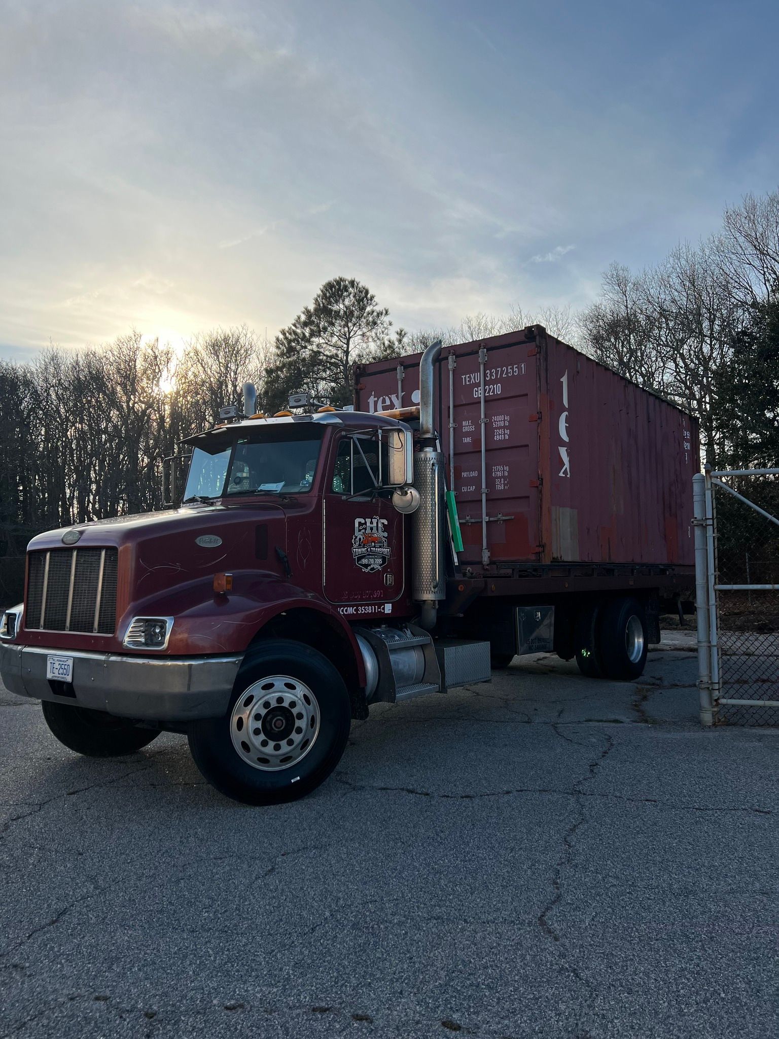 A red semi truck with a container on the back is parked in a gravel lot.