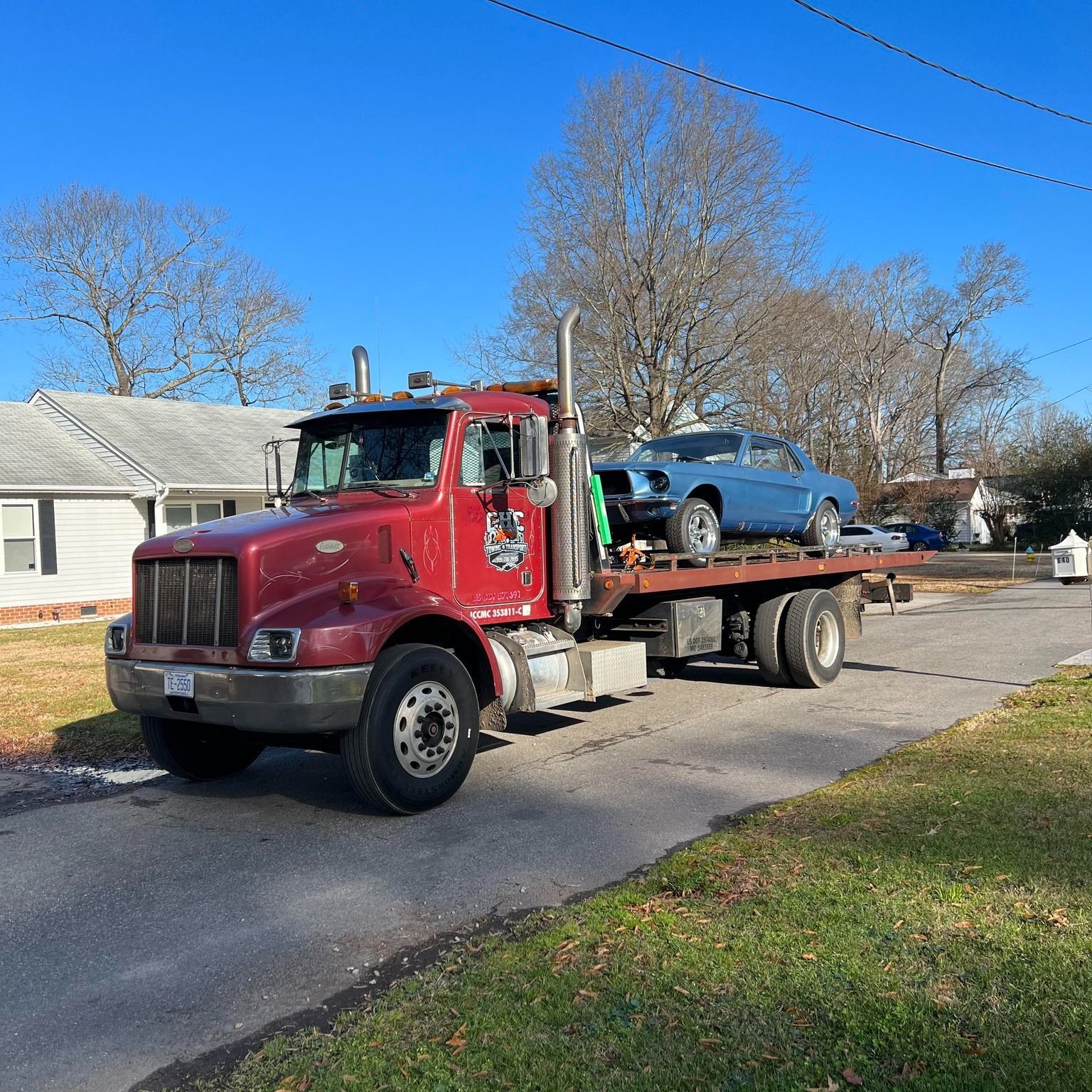 A red tow truck is carrying a blue car on its flatbed.