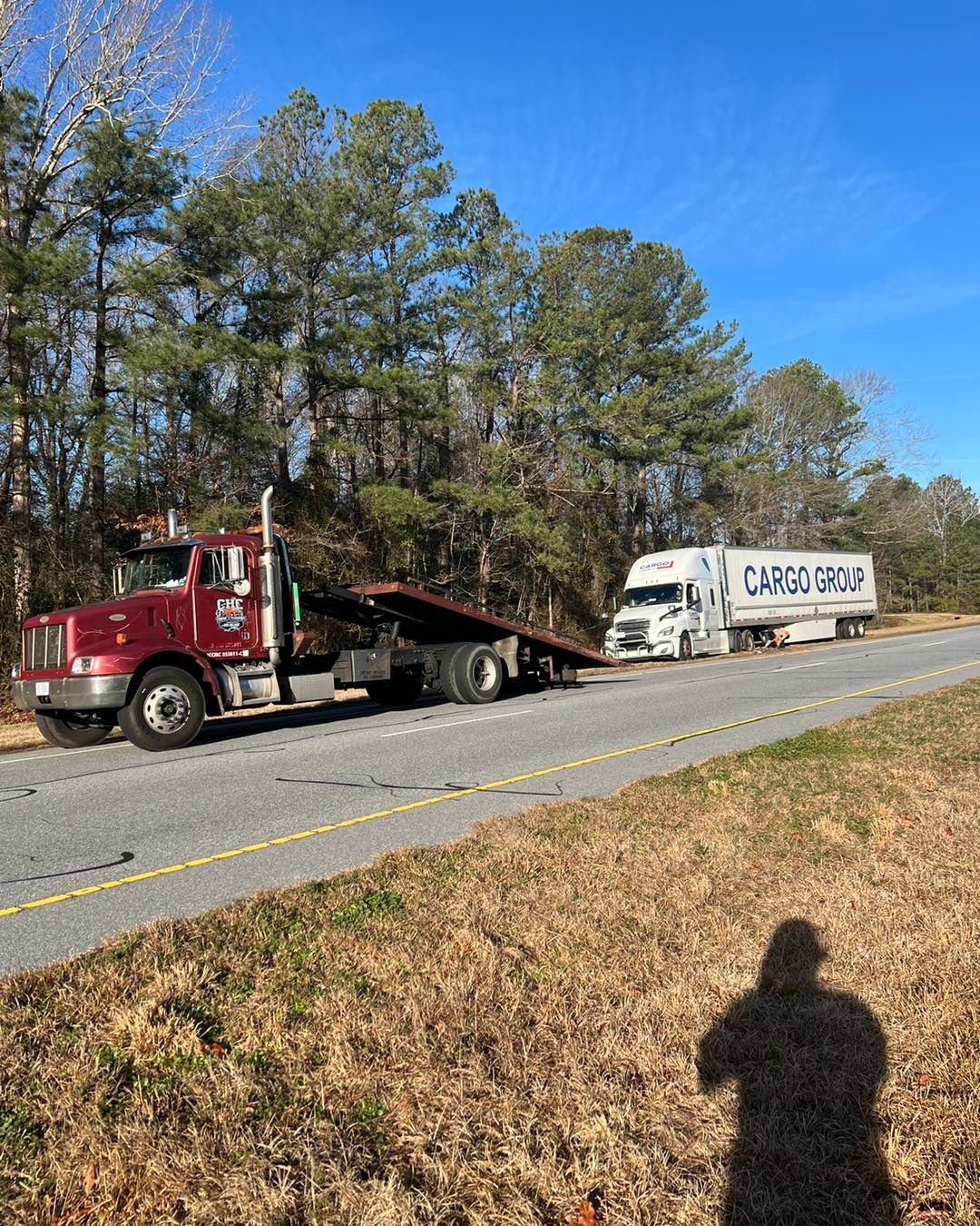 A red tow truck is driving down the road next to a white truck.
