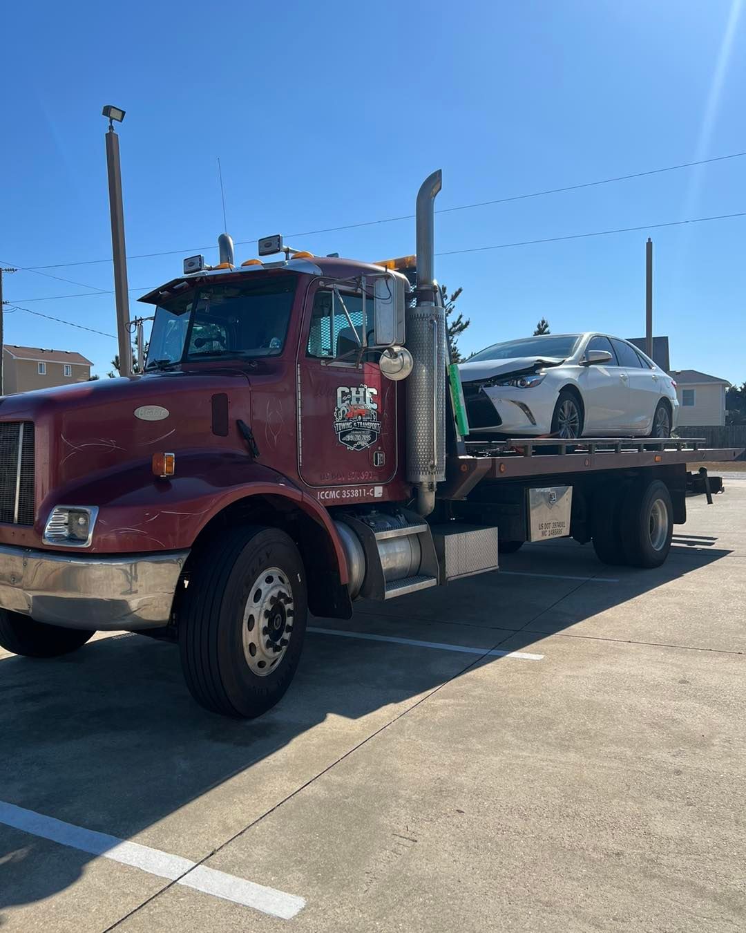 A red tow truck with a white car on the back is parked in a parking lot.