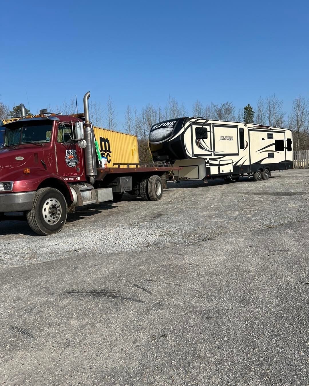 A red tow truck is towing a trailer in a gravel lot.