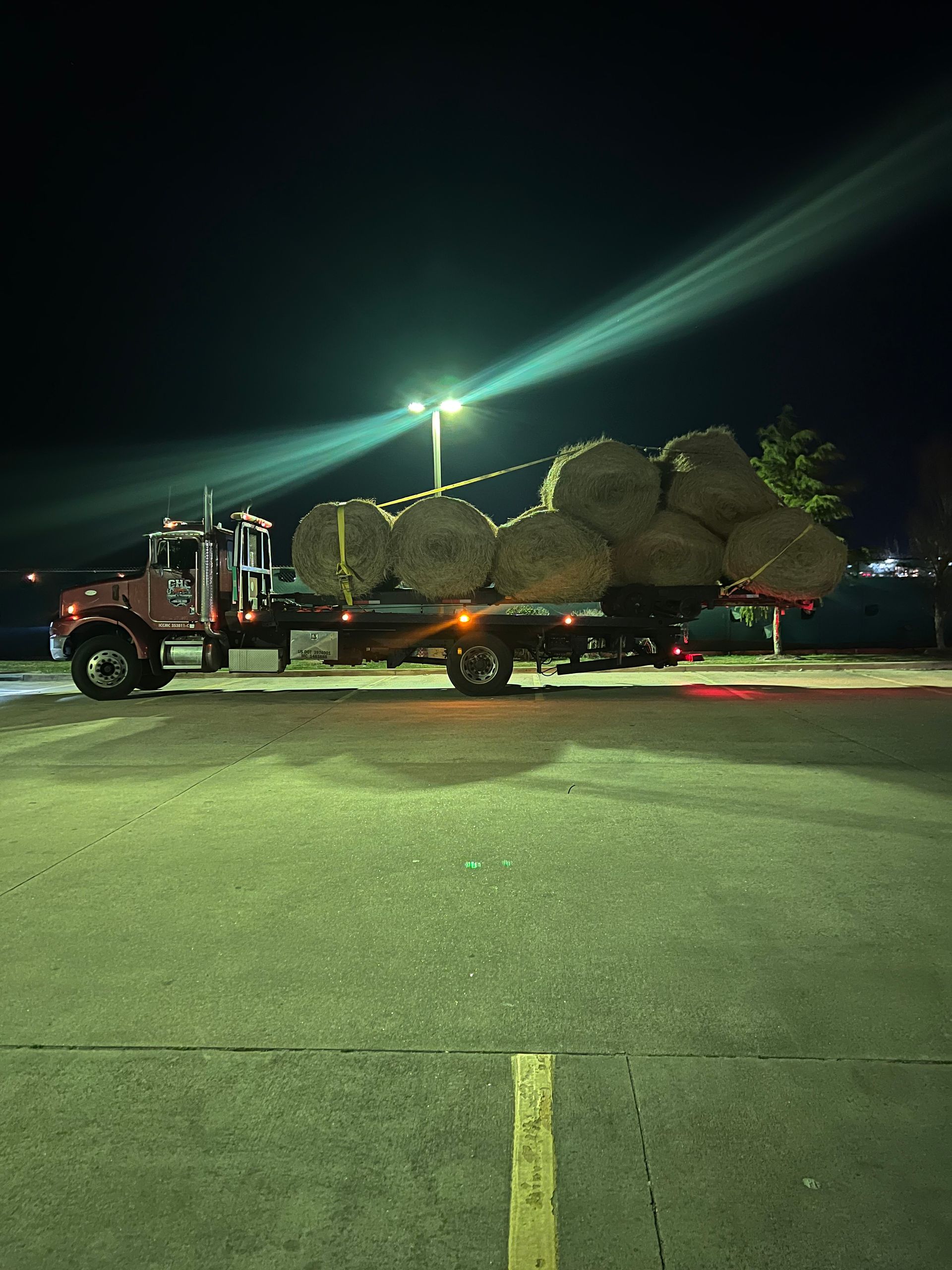 A truck is pulling a trailer full of hay bales at night.