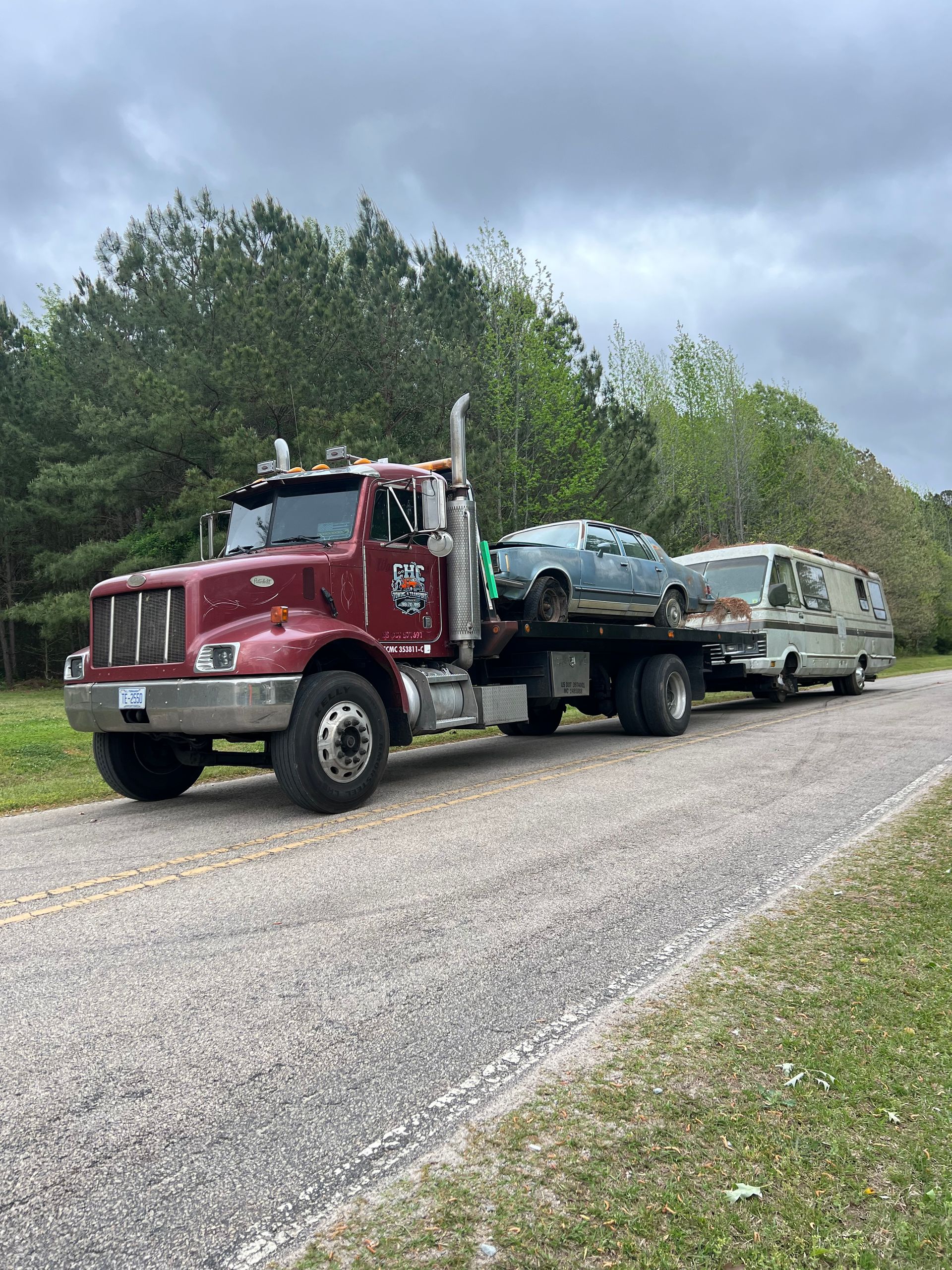 A red tow truck is towing a white van down a gravel road.