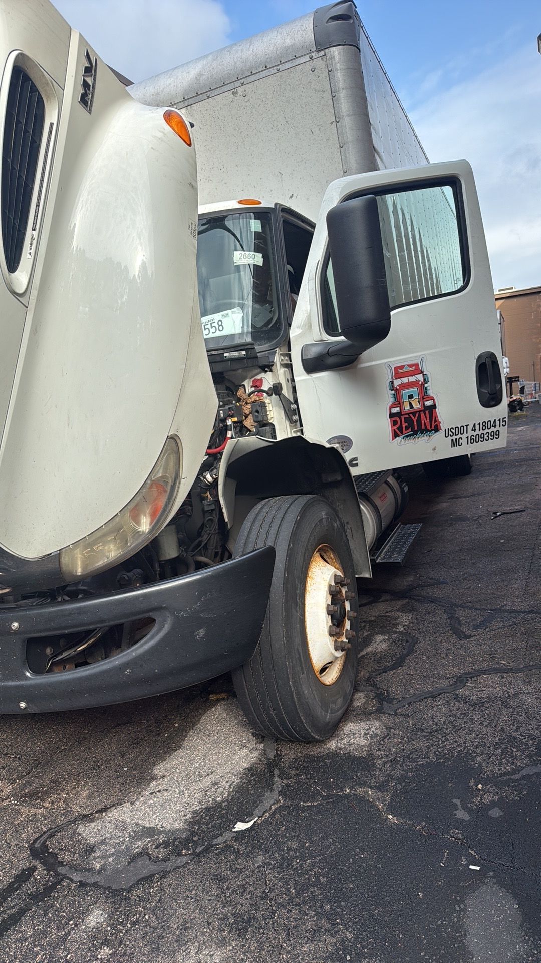 White delivery truck with open driver door and raised hood parked on a paved lot