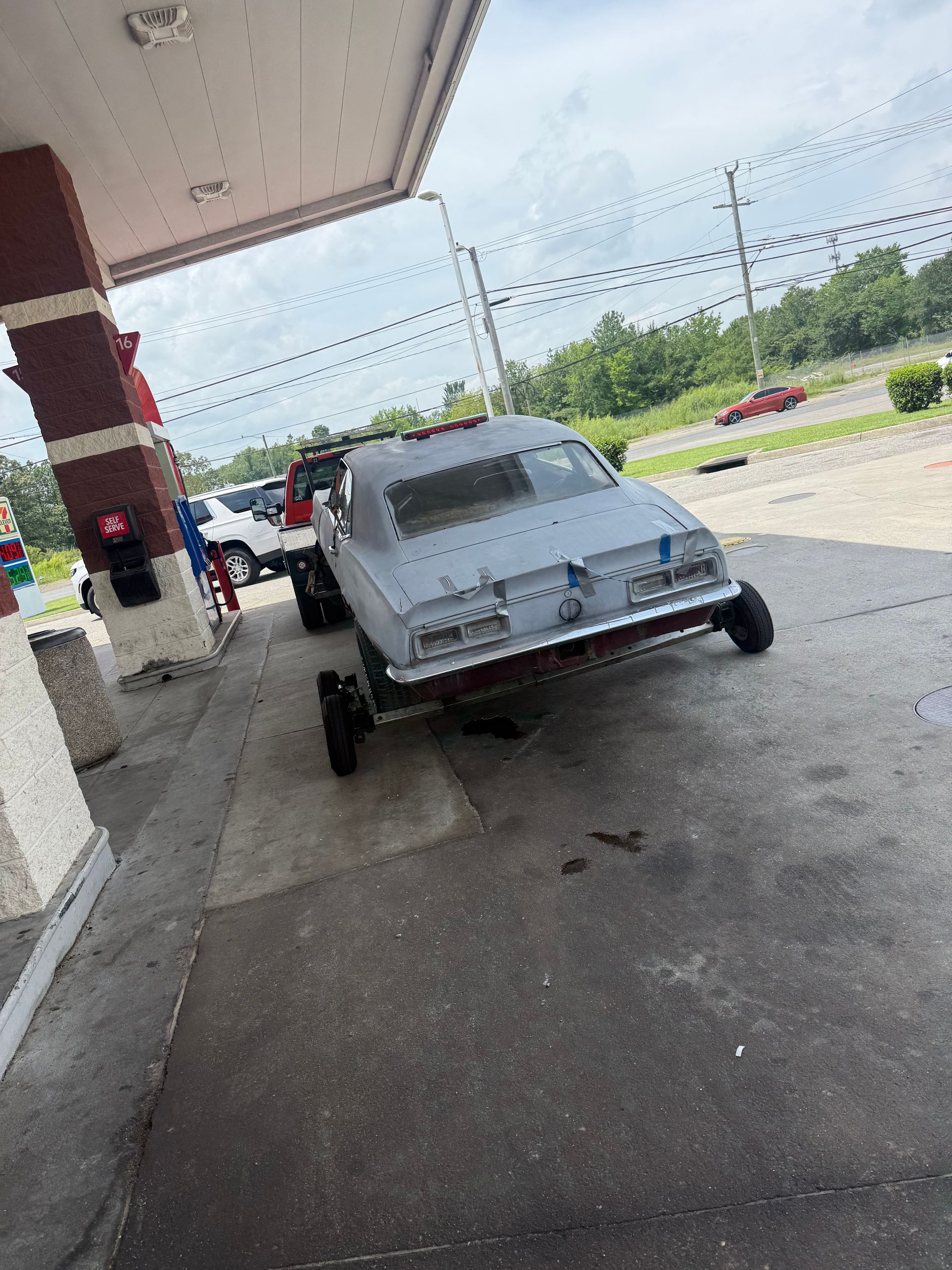 Trailer carrying a white vintage car outside a store under a covered walkway