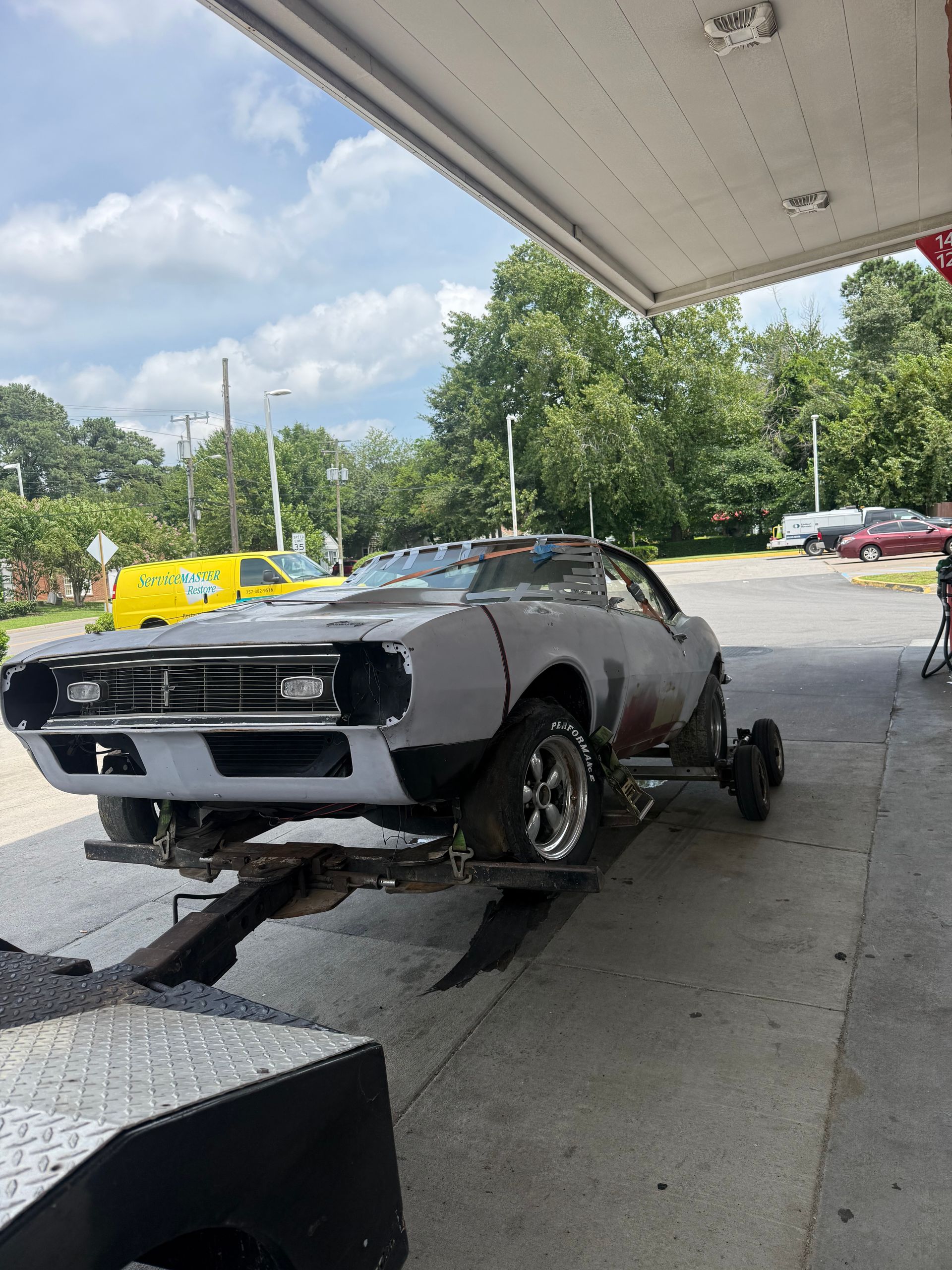 Damaged black muscle car on a tow truck at a gas station under a canopy