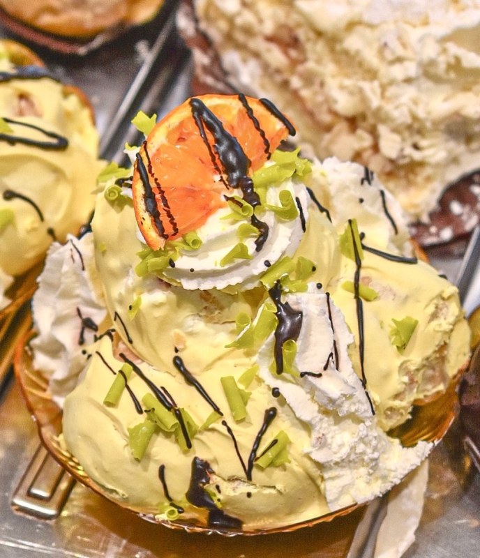Dolce giallo con panna montata, fetta d'arancia e glassa di cioccolato.