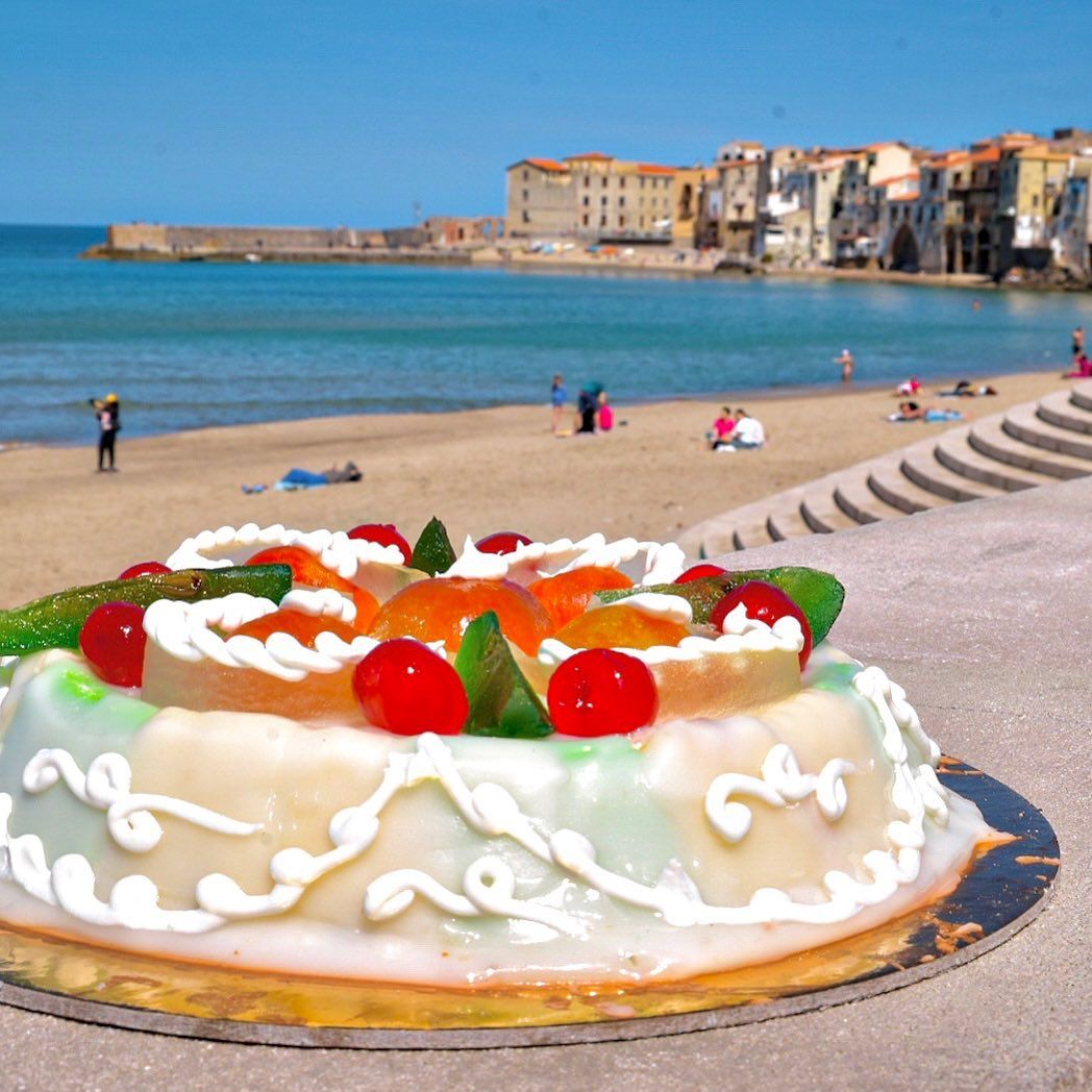Torta con frutta candita sulla spiaggia di fronte a una città costiera.