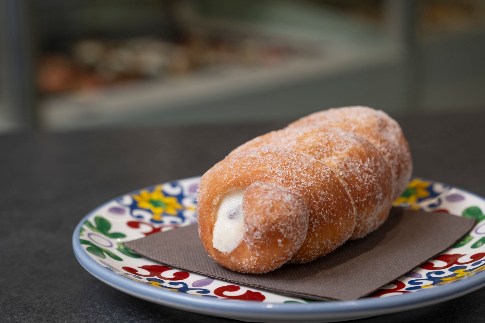 Pasta cannolo con ripieno di crema su un piatto colorato, spolverata di zucchero.