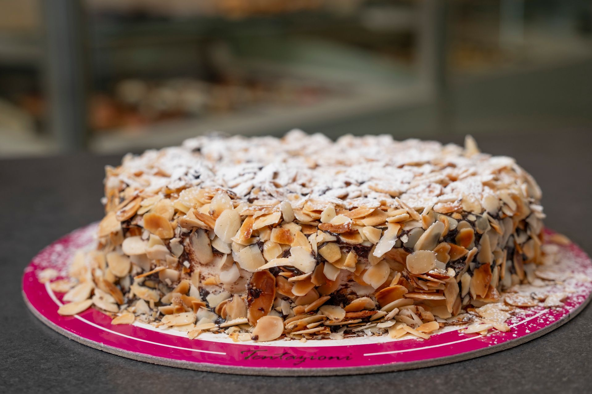 Torta con lamelle di mandorle, spolverata di zucchero a velo, su un piatto rosa.