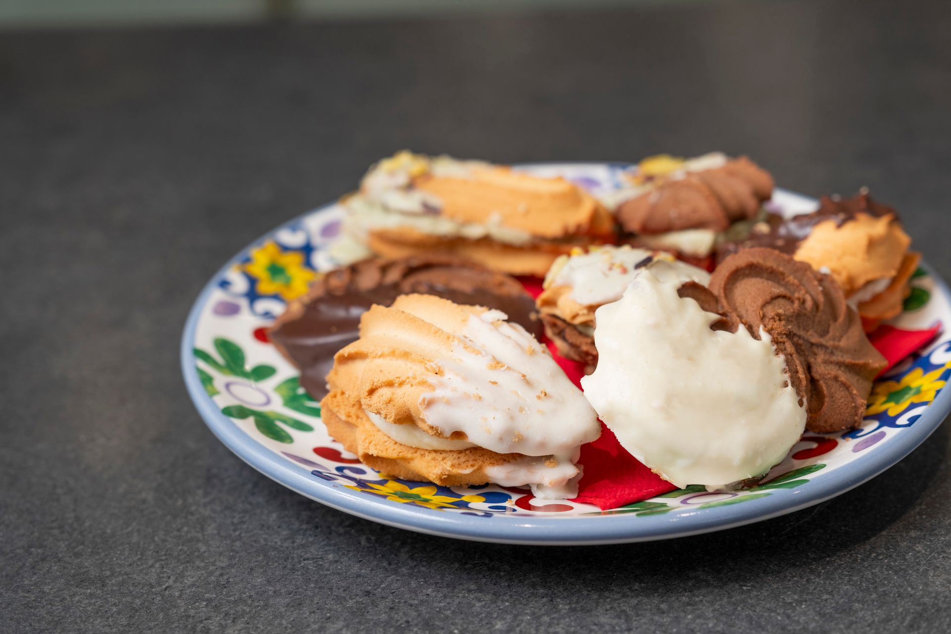 Biscotti su un piatto decorato, un mix di cioccolato e vaniglia, su un piano di lavoro scuro.