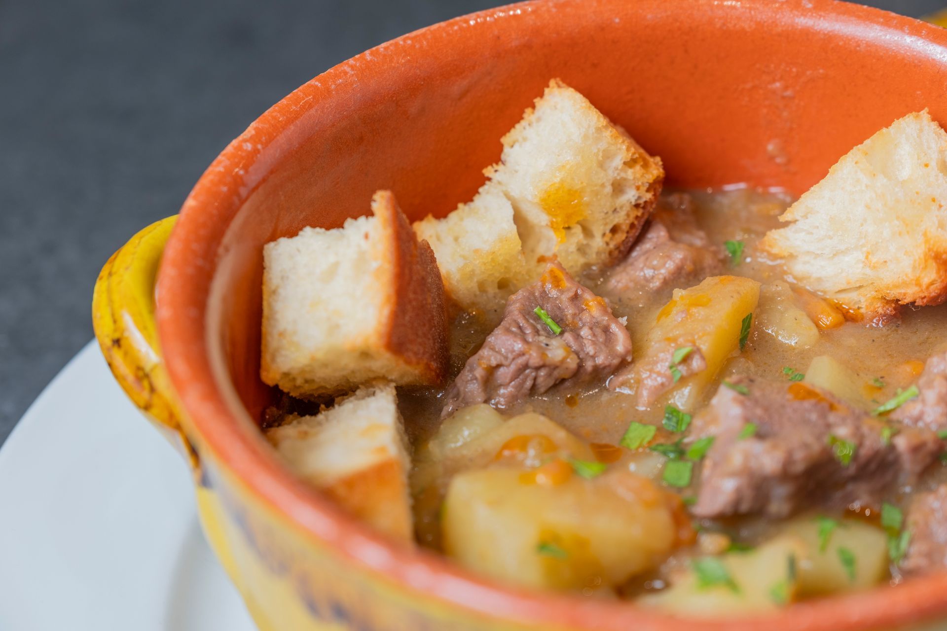 Spezzatino di manzo con patate e crostini di pane tostato in una rustica ciotola arancione.