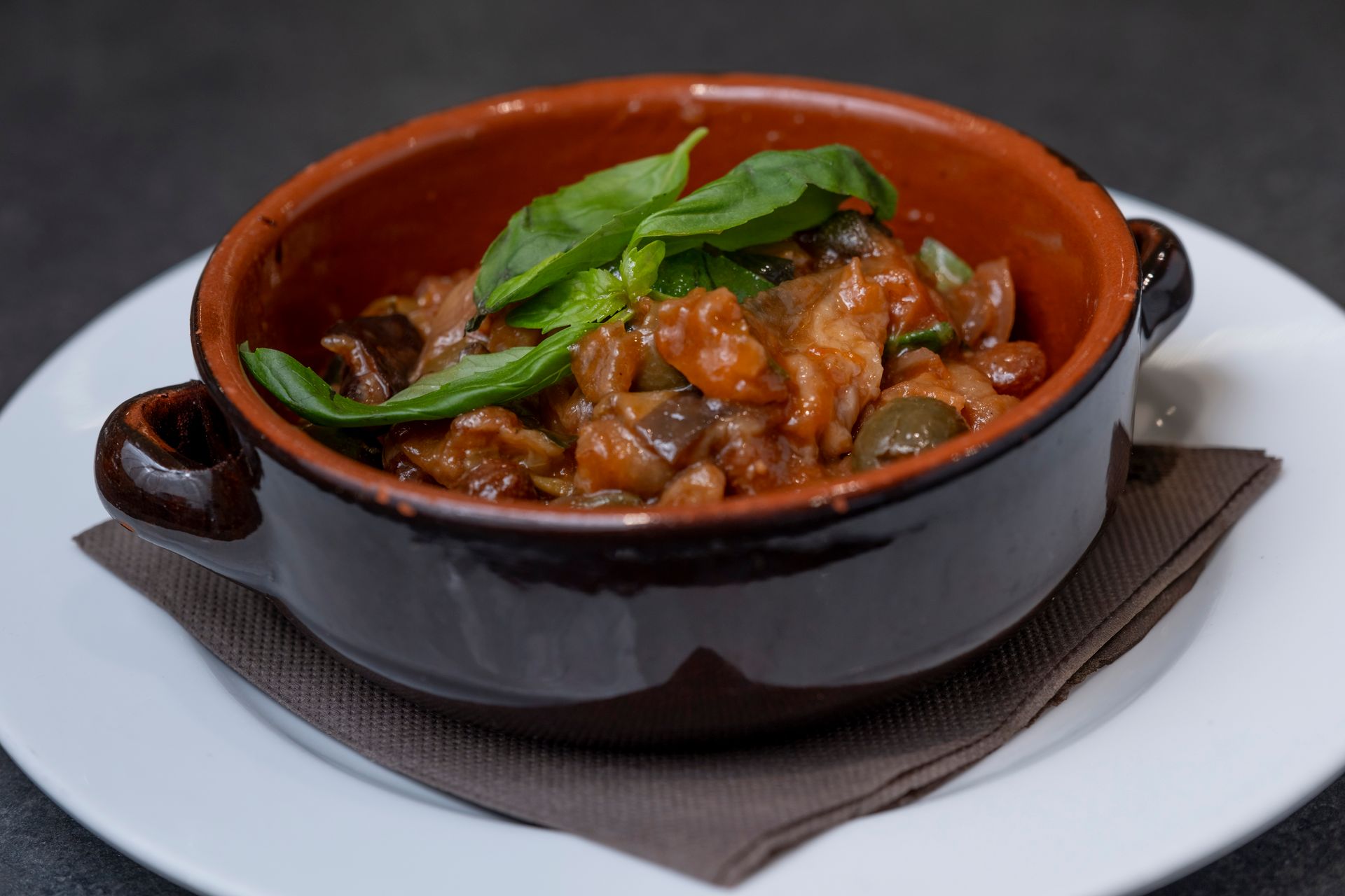 Cuocere a fuoco lento in una ciotola marrone, guarnire con basilico su un piatto bianco.