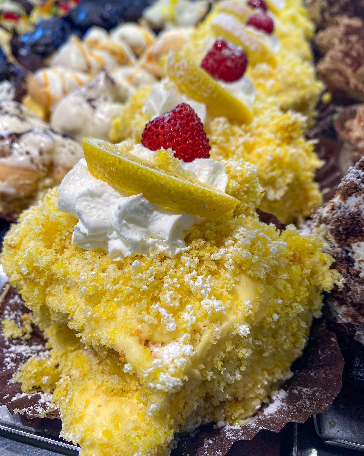 Fette di torta al limone guarnite con panna montata, lamponi e scorza di limone.