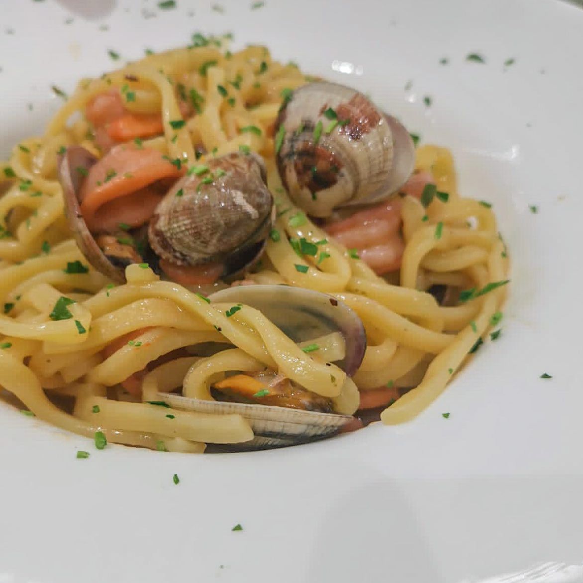 Pasta con le vongole, guarnita con prezzemolo, in una ciotola bianca.