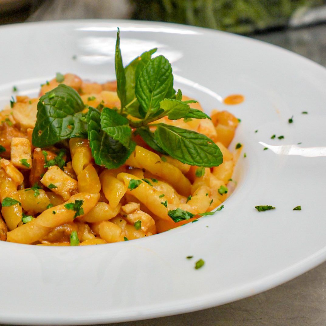 Piatto di pasta con sugo rosso, guarnito con menta e prezzemolo, in una ciotola bianca.