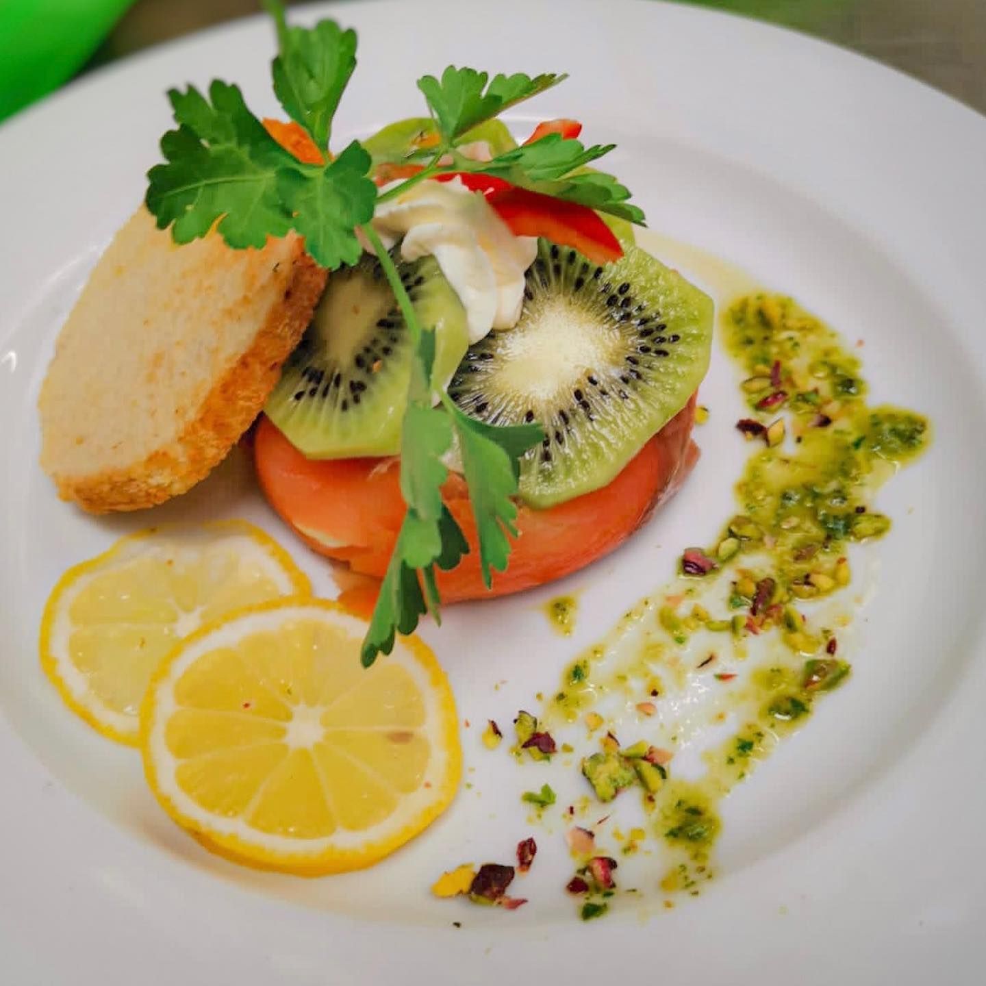 Insalata con kiwi, pomodoro, limone e pesto su un piatto bianco.