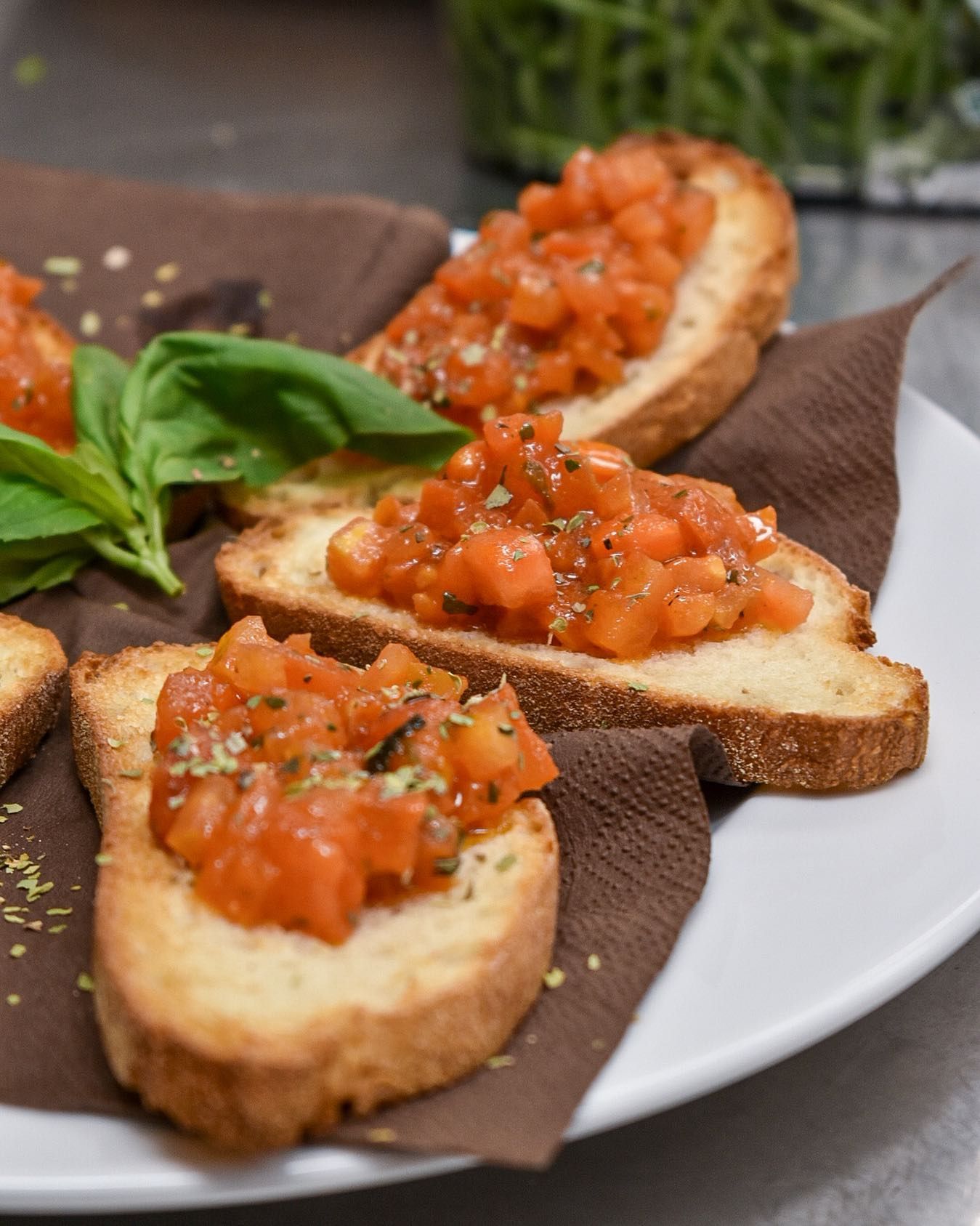 Bruschetta: fette di pane tostato condite con pomodori a cubetti, erbe aromatiche e basilico su un piatto.