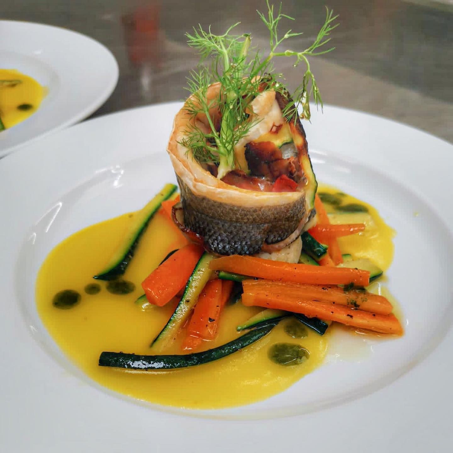 Salmone arrotolato con verdure e salsa gialla su un piatto bianco, guarnito con aneto.