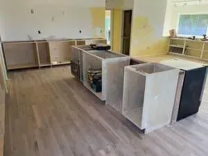 Kitchen undergoing renovation with wooden floorboards and newly installed unfinished wooden cabinetry and kitchen island.