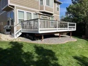 A beige two-story house with a white-railed deck elevated above a gravel patio and a grassy backyard.
