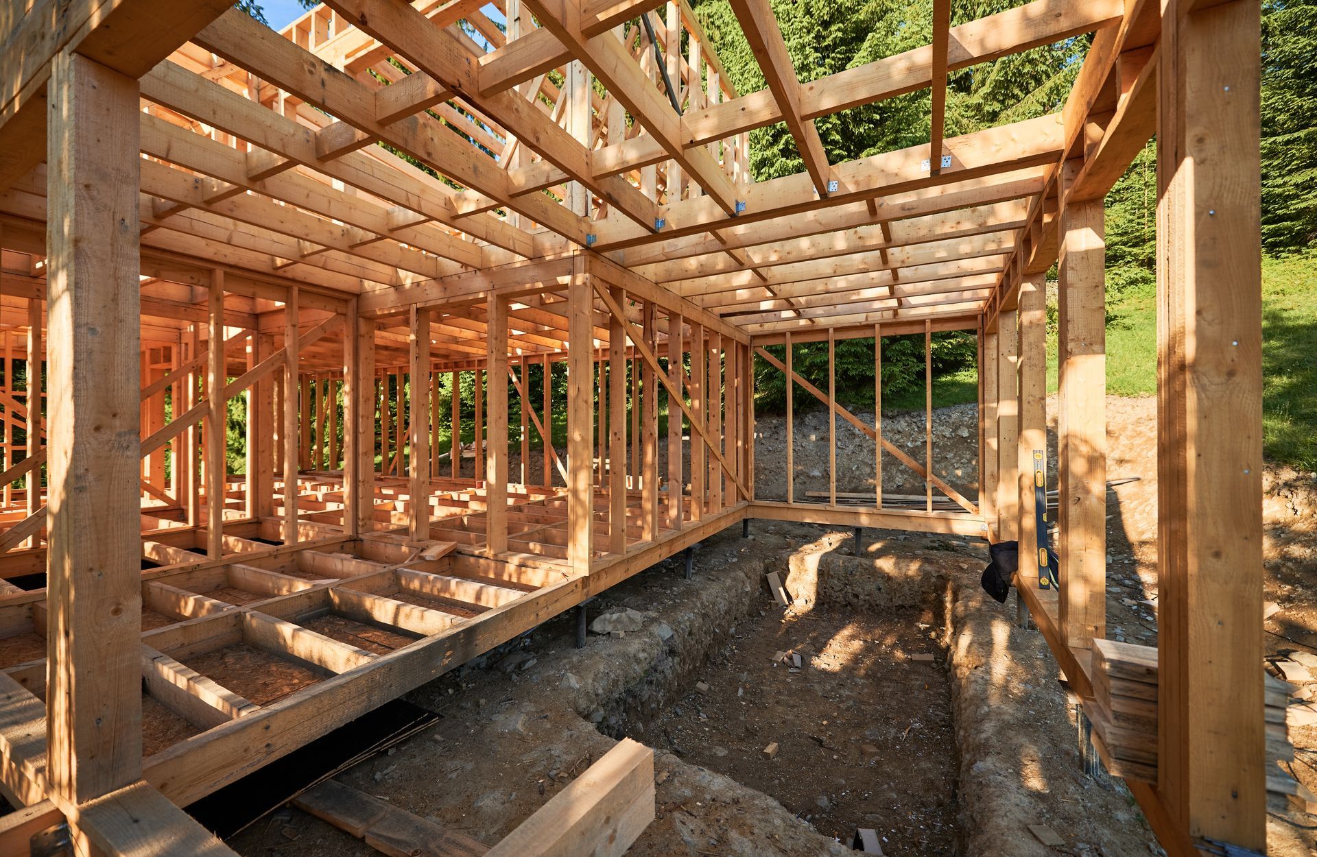 Wooden framing and floor joists for a building under construction, set above an excavated dirt foundation.