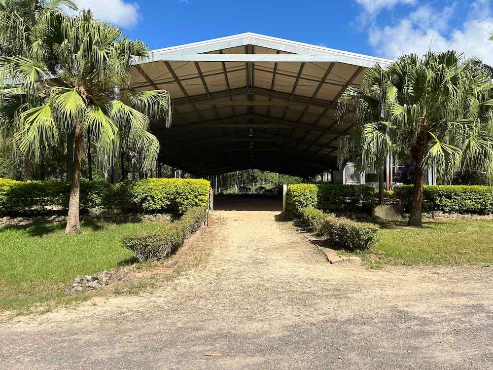 A Large Building With a White Roof is Surrounded by Palm Trees and Bushes — Merrypark Equestrian Centre In Eumundi, QLD
