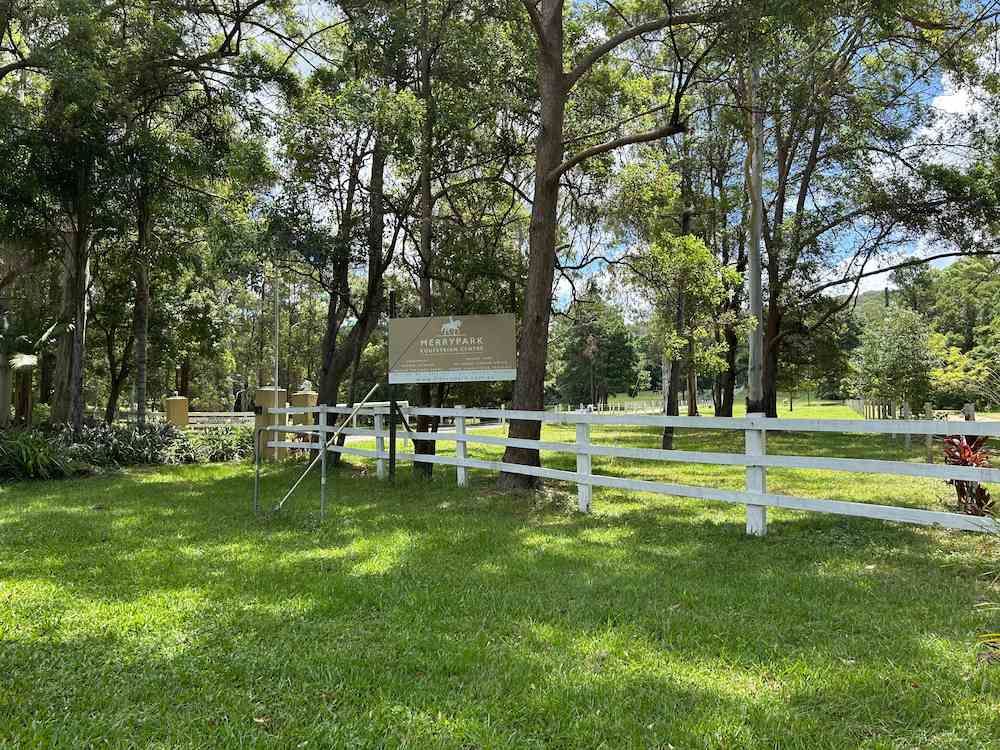 A White Fence Surrounds a Grassy Field With Trees in the Background — Merrypark Equestrian Centre In Eumundi, QLD