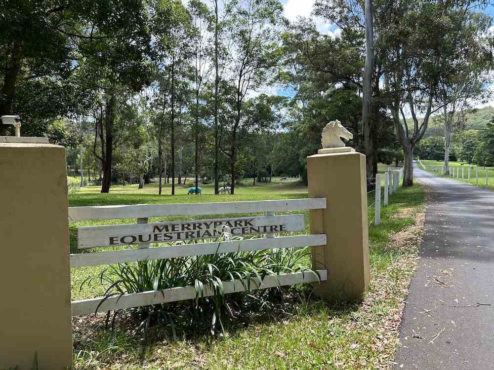 A White Fence With a Horse on Top of It is Surrounded by Grass and Trees — Merrypark Equestrian Centre In Eumundi, QLD