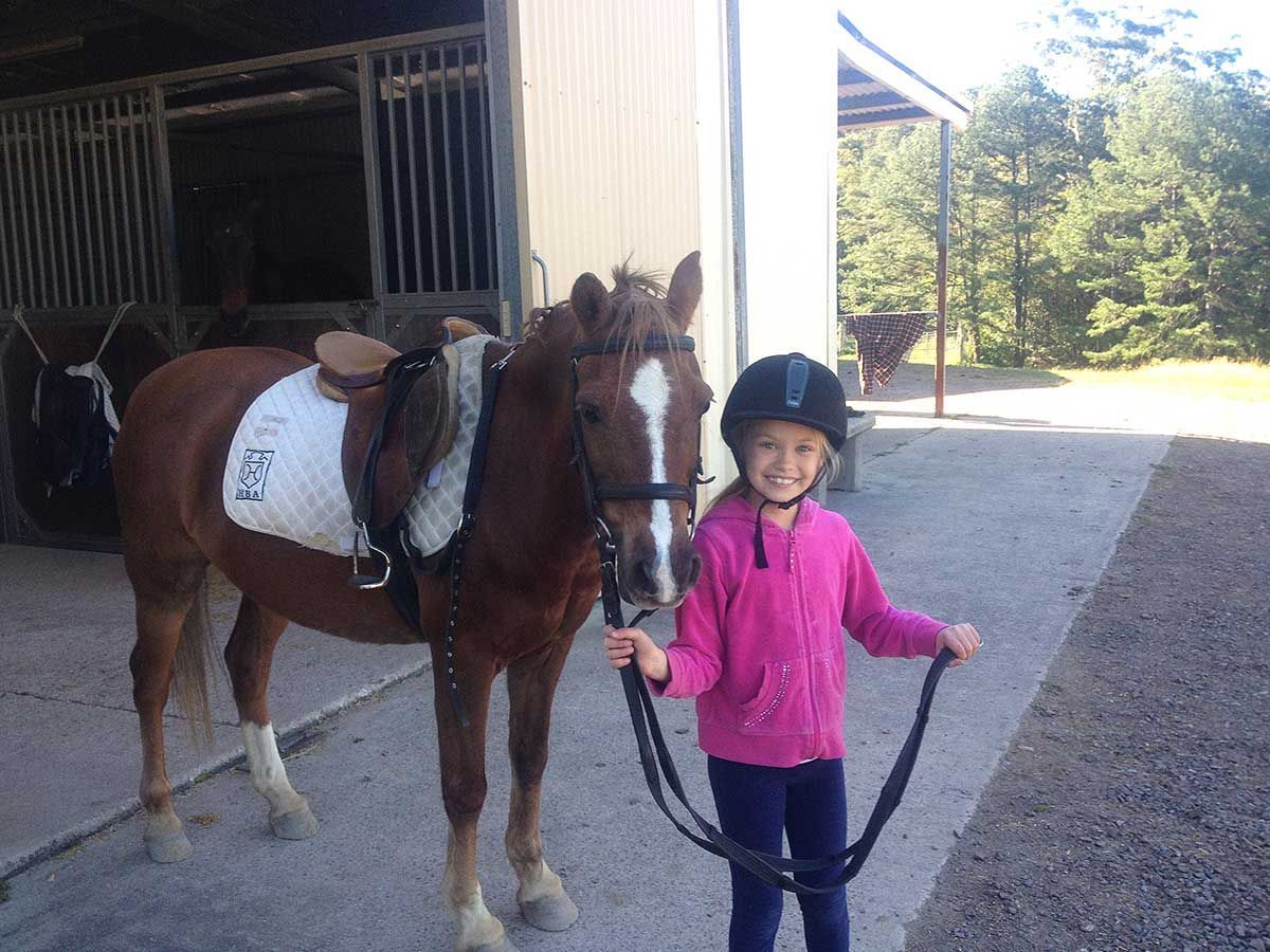 A Little Girl In A Pink Jacket Is Standing Next To A Brown Horse — Merrypark Equestrian Centre In Eumundi, QLD