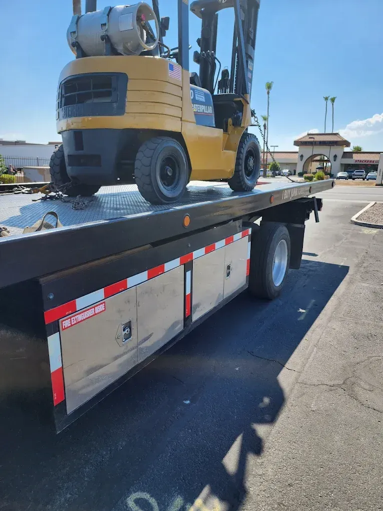 Yellow forklift on a flatbed tow truck. Bright sunlight.