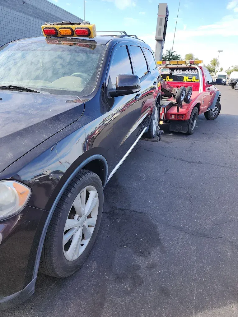 Black SUV being towed by a red tow truck in a parking lot on a sunny day.