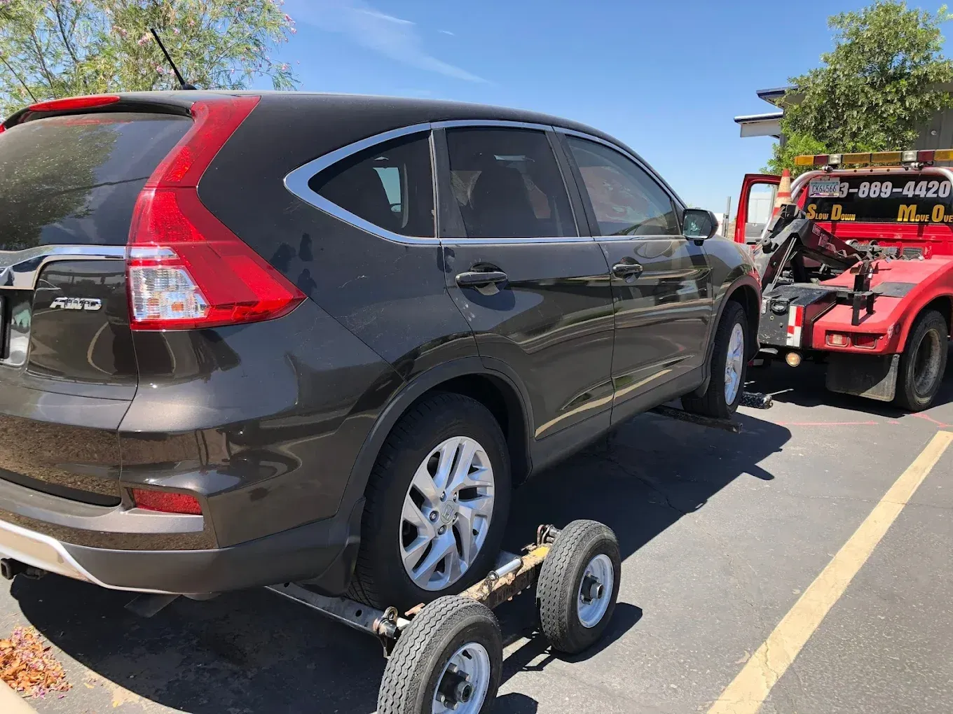 Black SUV being towed by a red tow truck on a sunny day.