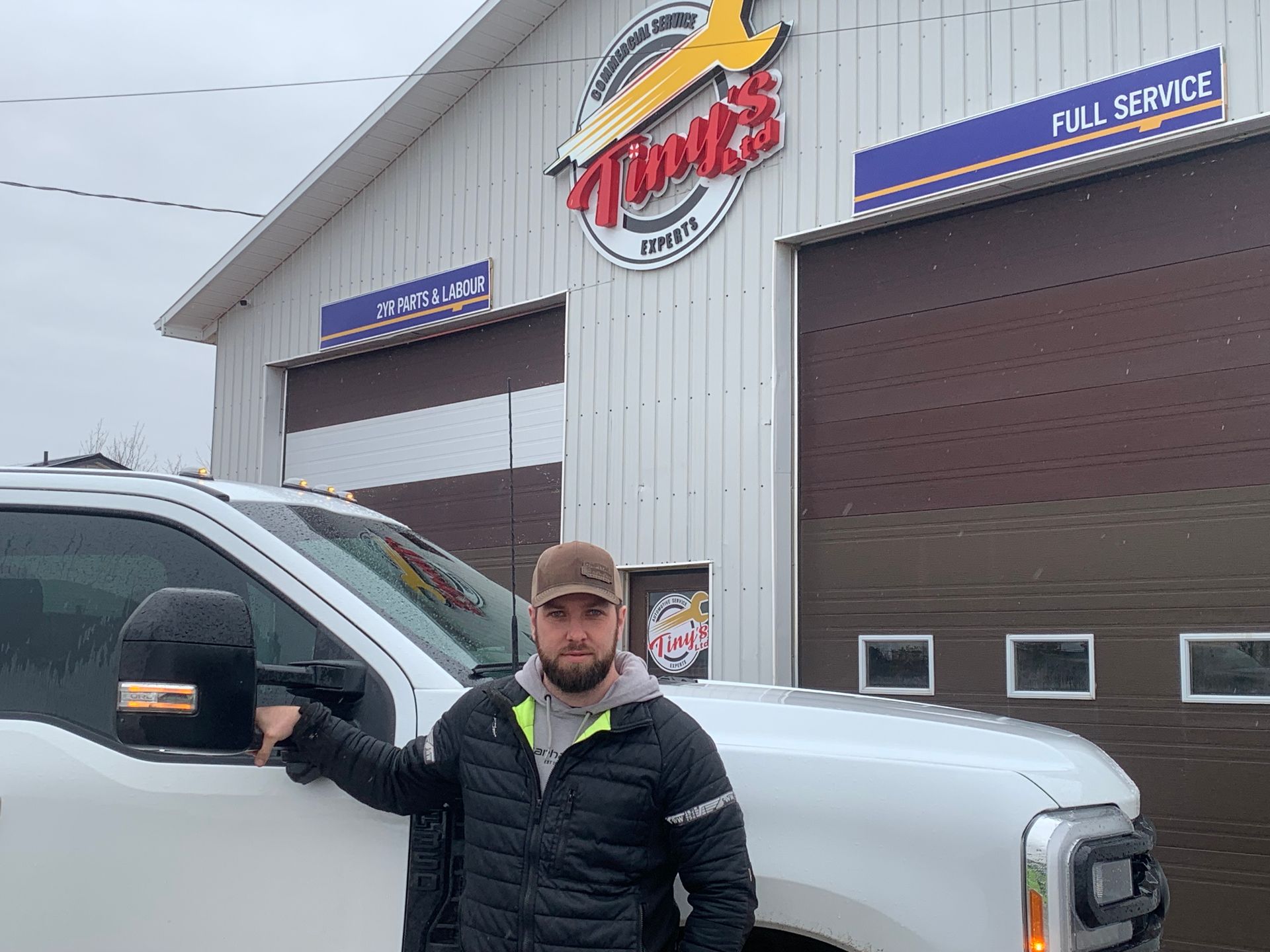 A man is standing next to a white truck in front of a garage. | Tiny's Automotive