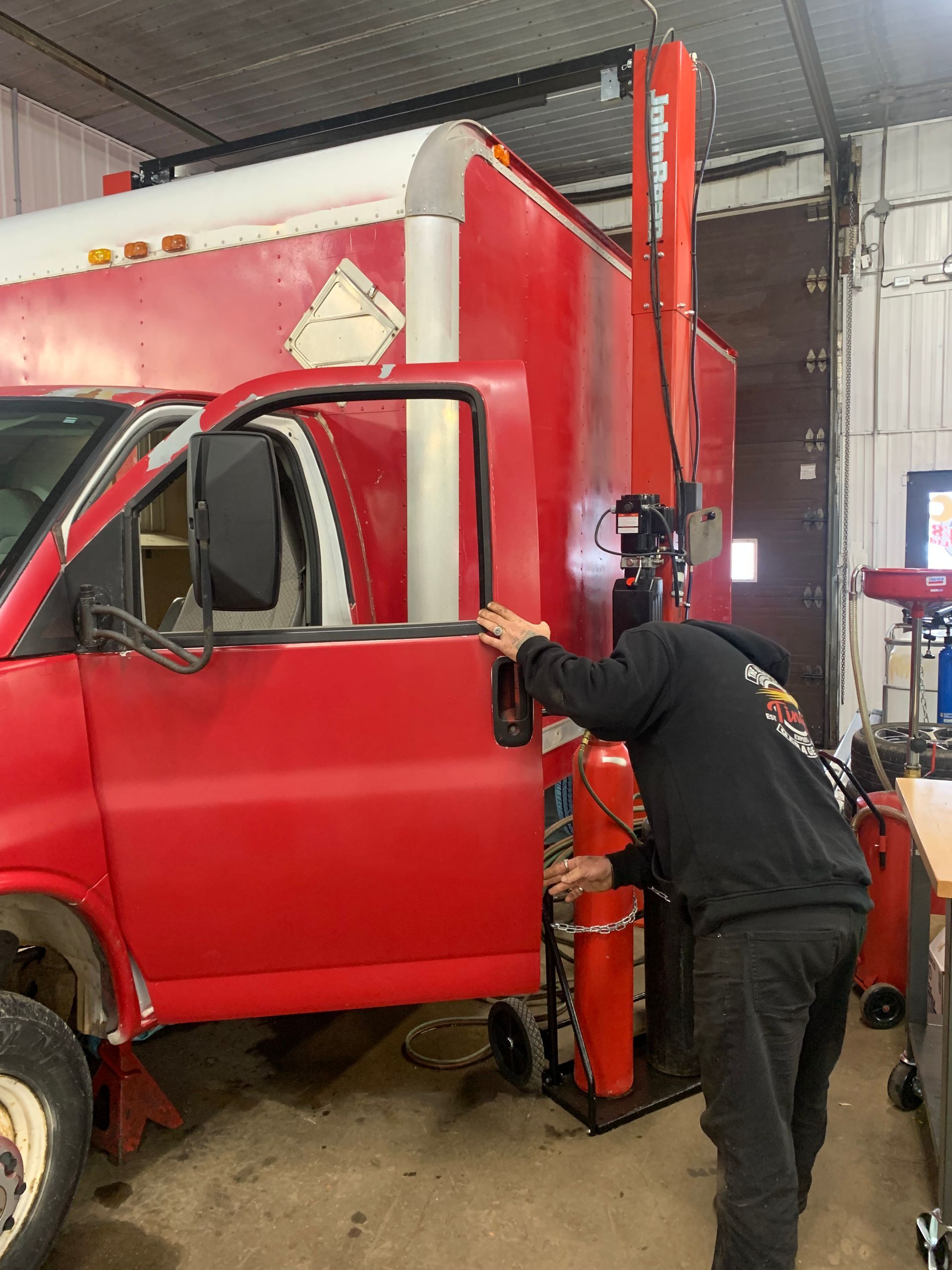 A man is working on a red truck in a garage. | Tiny's Automotive