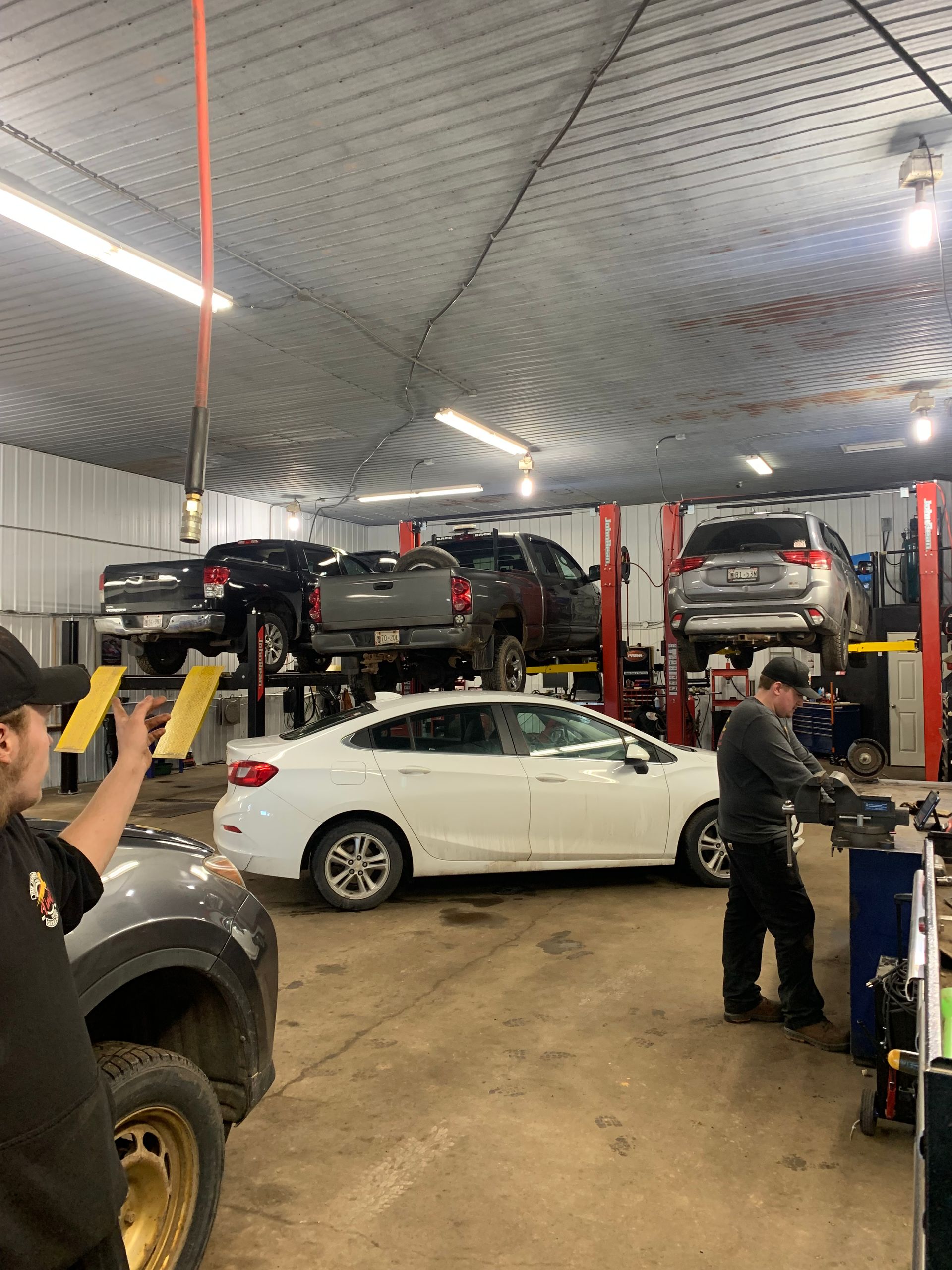 A man is standing in a garage with cars on lifts. | Tiny's Automotive