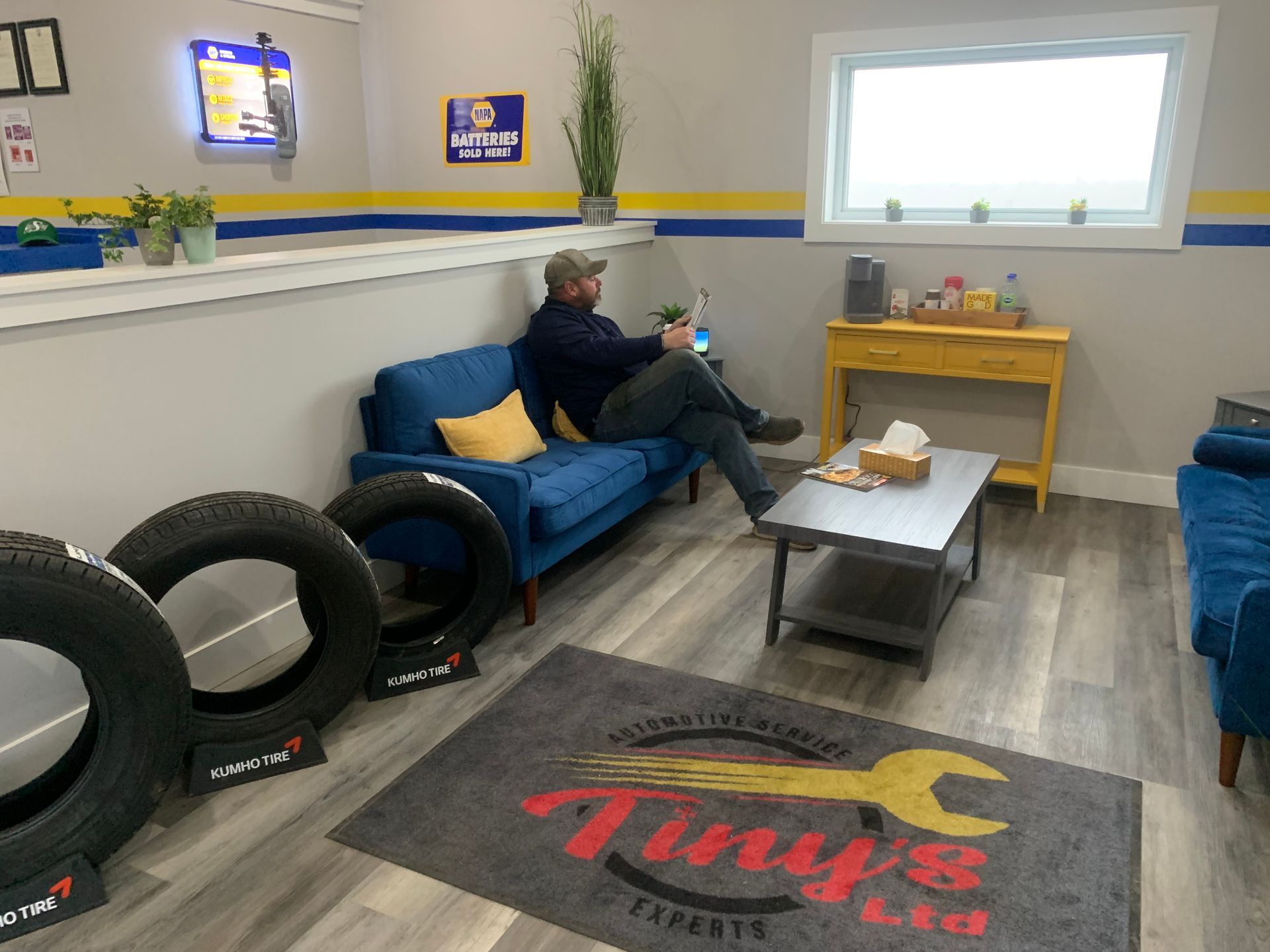 A man is sitting on a blue couch in a waiting room. | Tiny's Automotive