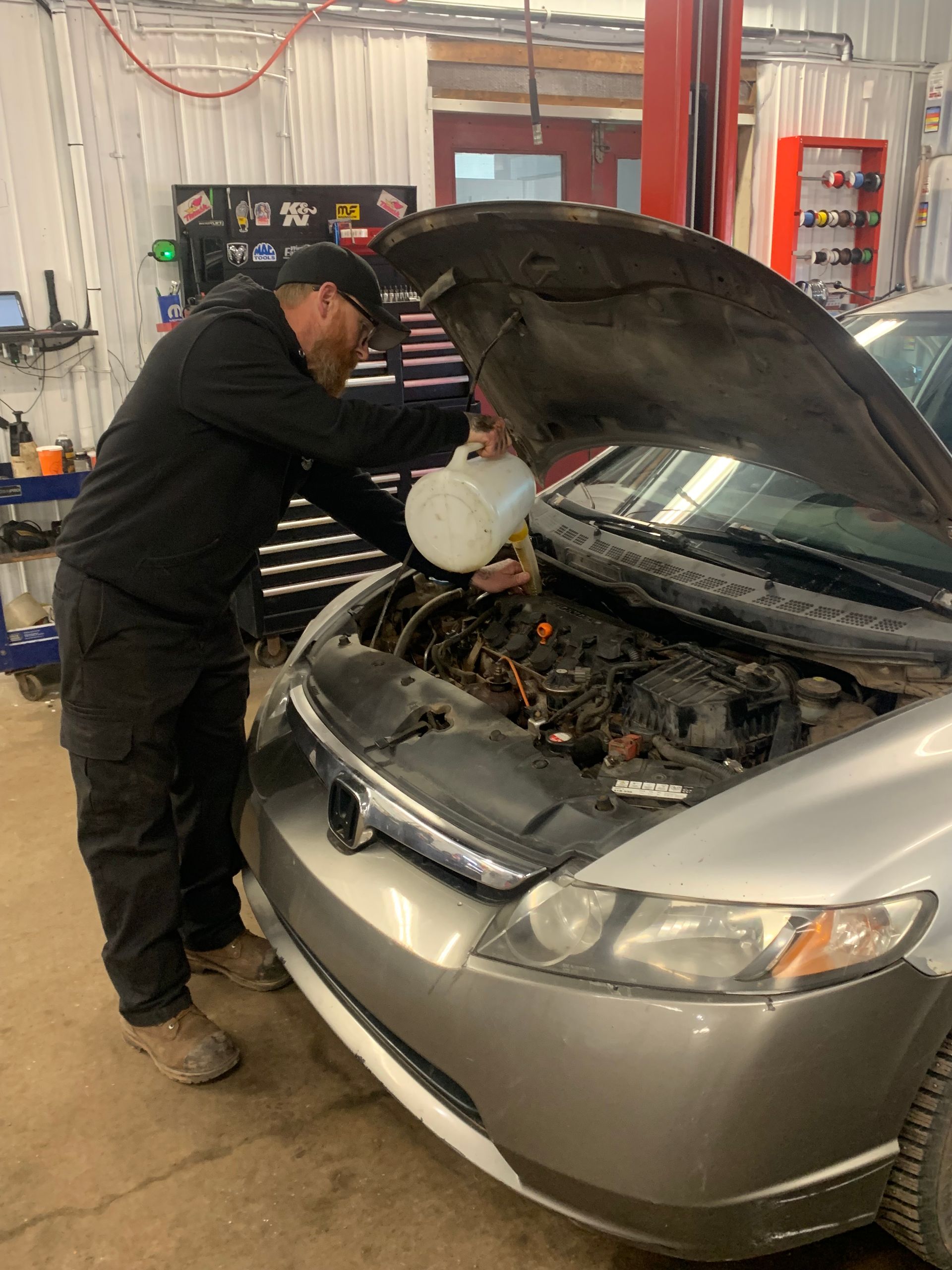 A man is pouring oil into the engine of a car. | Tiny's Automotive