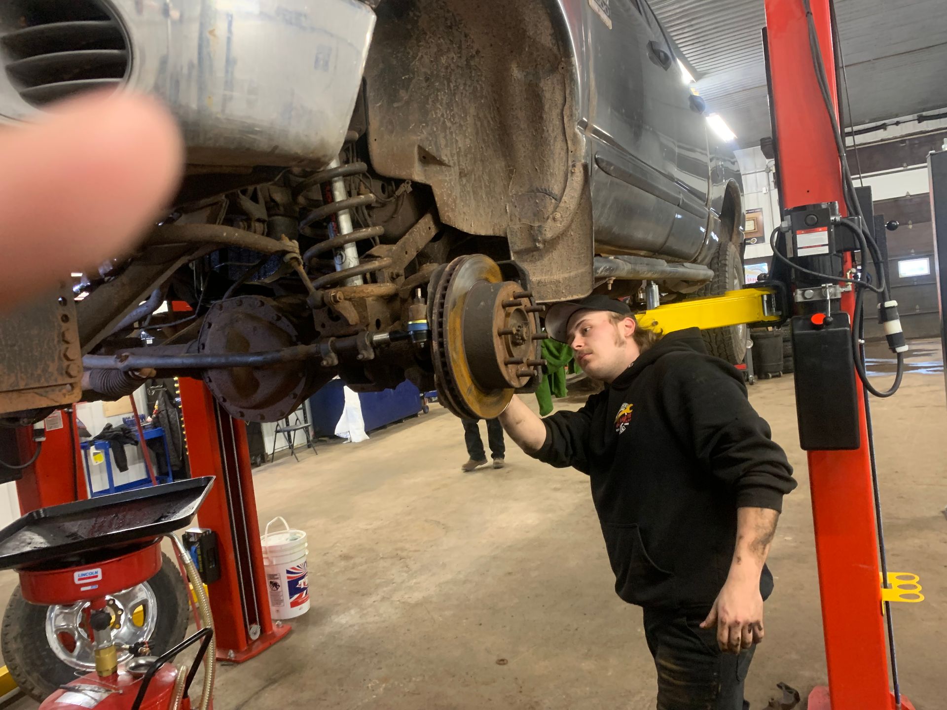 A man is working on a car on a lift in a garage. | Tiny's Automotive