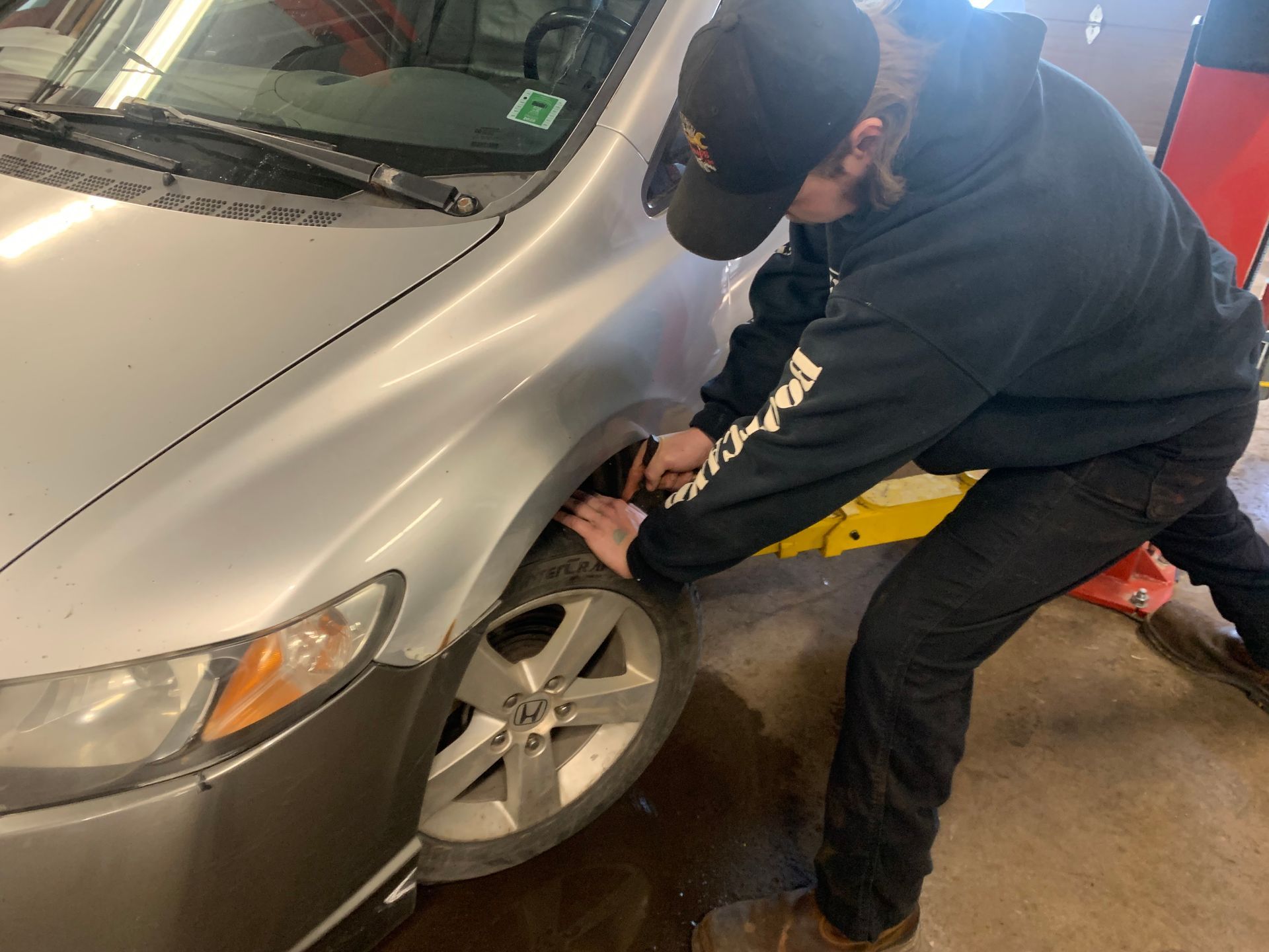 A man is changing a tire on a car in a garage. | Tiny's Automotive