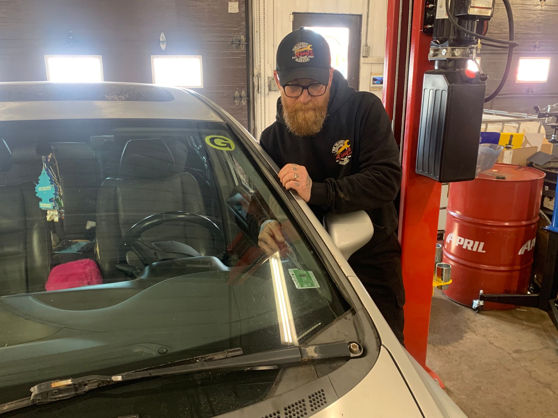 A man is working on a car windshield in a garage. | Tiny's Automotive