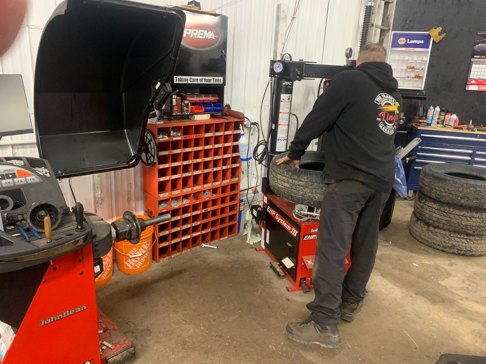 A man is standing next to a tire balancing machine in a garage. | Tiny's Automotive