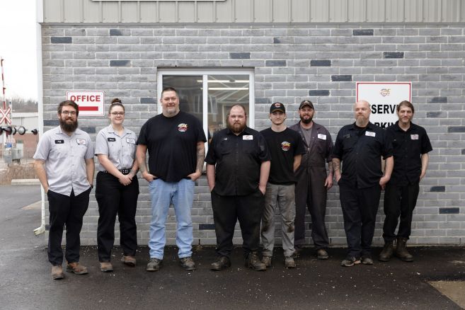 A group of people standing in front of a brick building. | Tiny's Automotive
