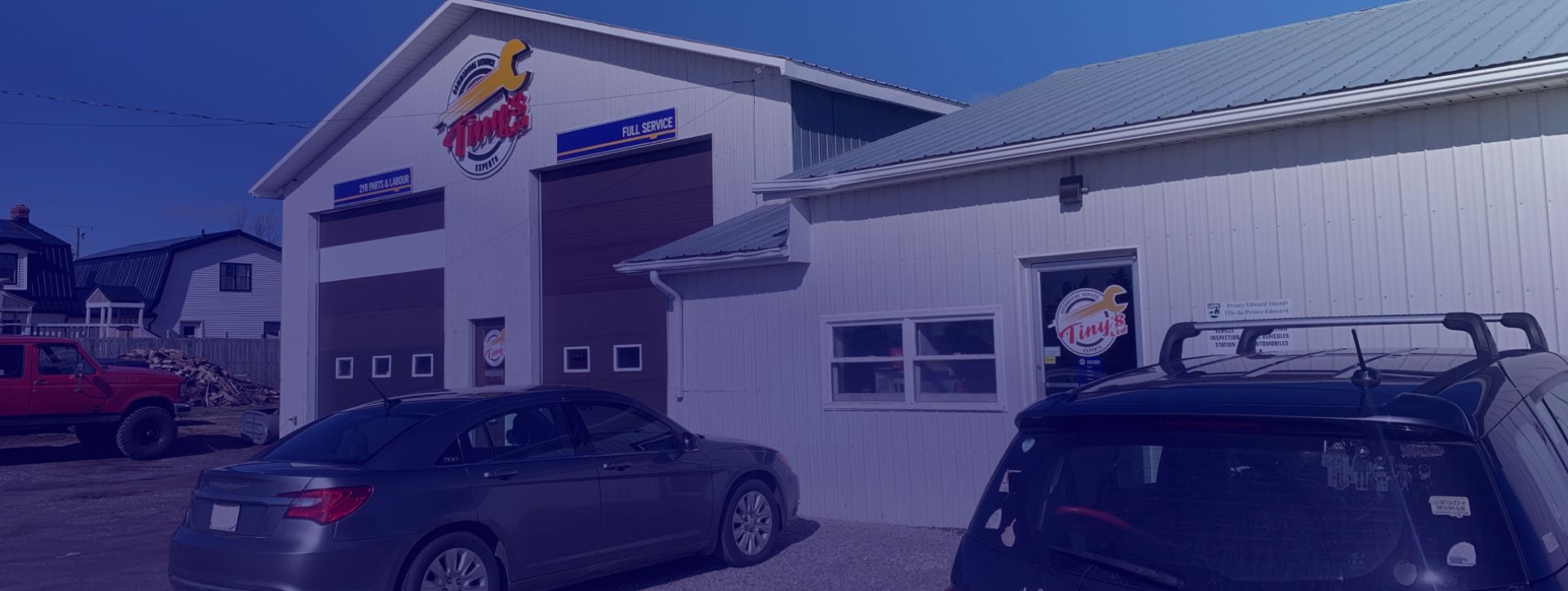 A white building with a car parked in front of it. | Tiny's Automotive