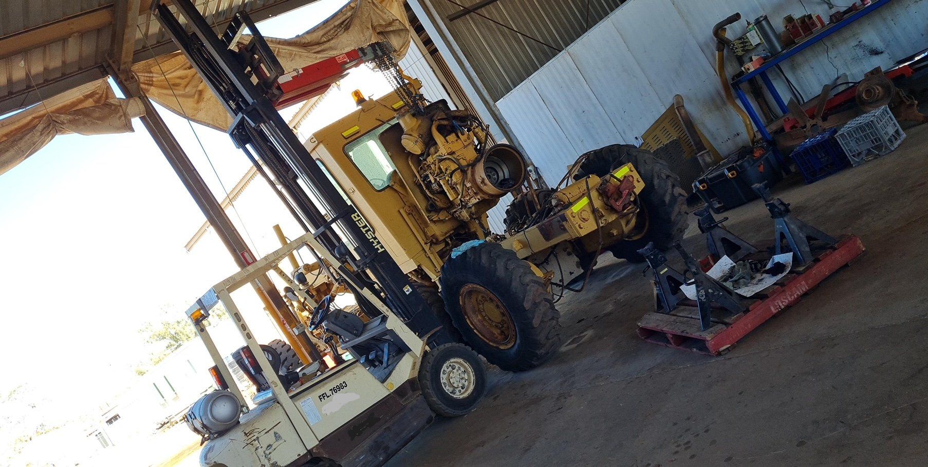 A forklift is sitting in a garage next to a tractor- Central Australian Sidelifter Haulage In Braitling NT
