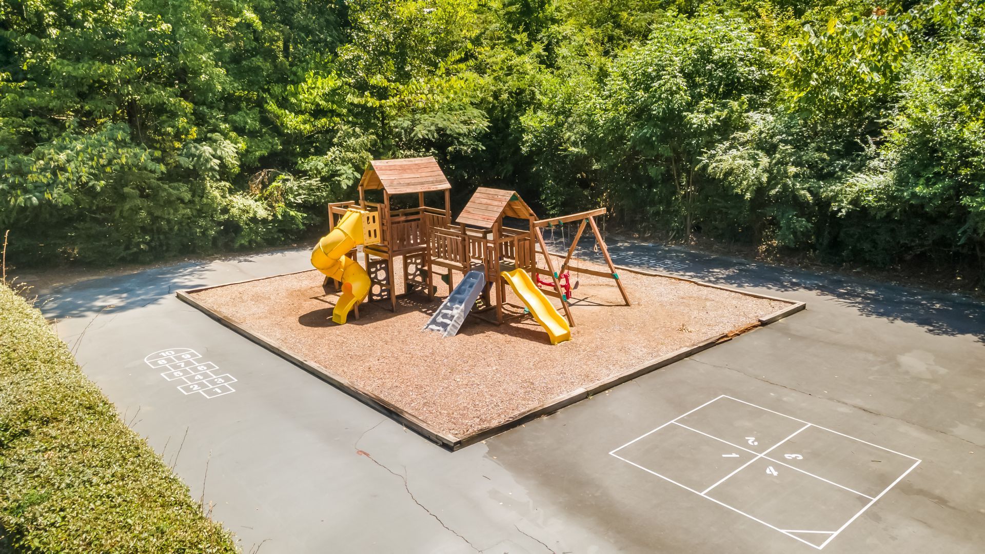 An aerial view of a playground in a parking lot surrounded by trees.