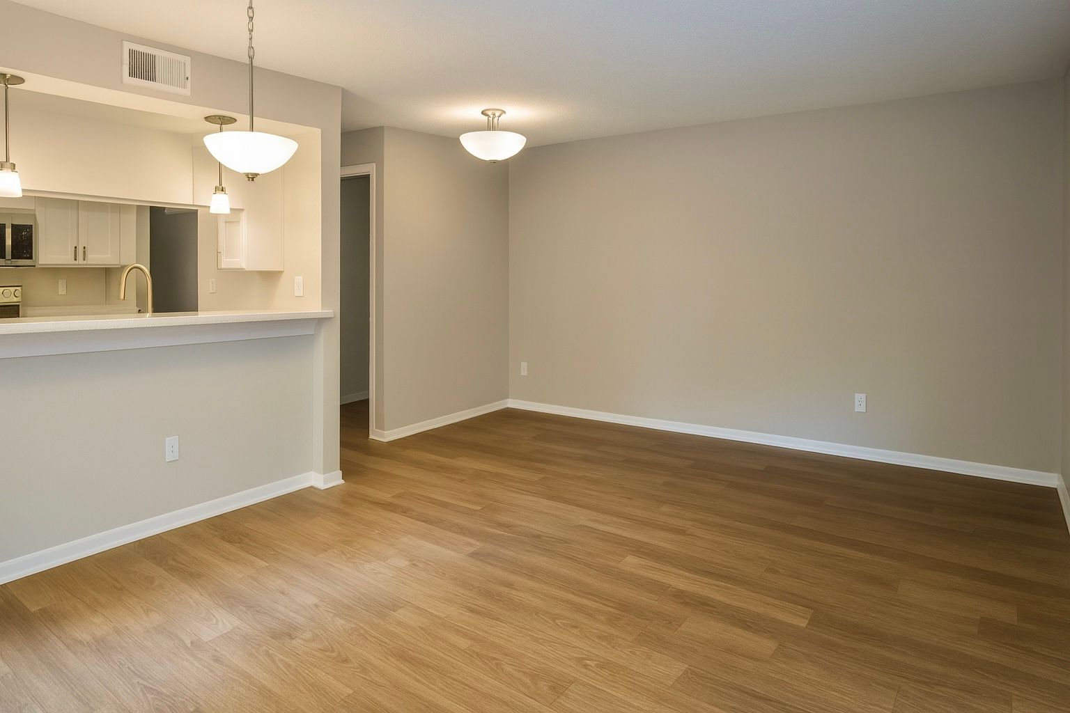 Empty living room with light wood floors, beige walls, and overhead lighting.