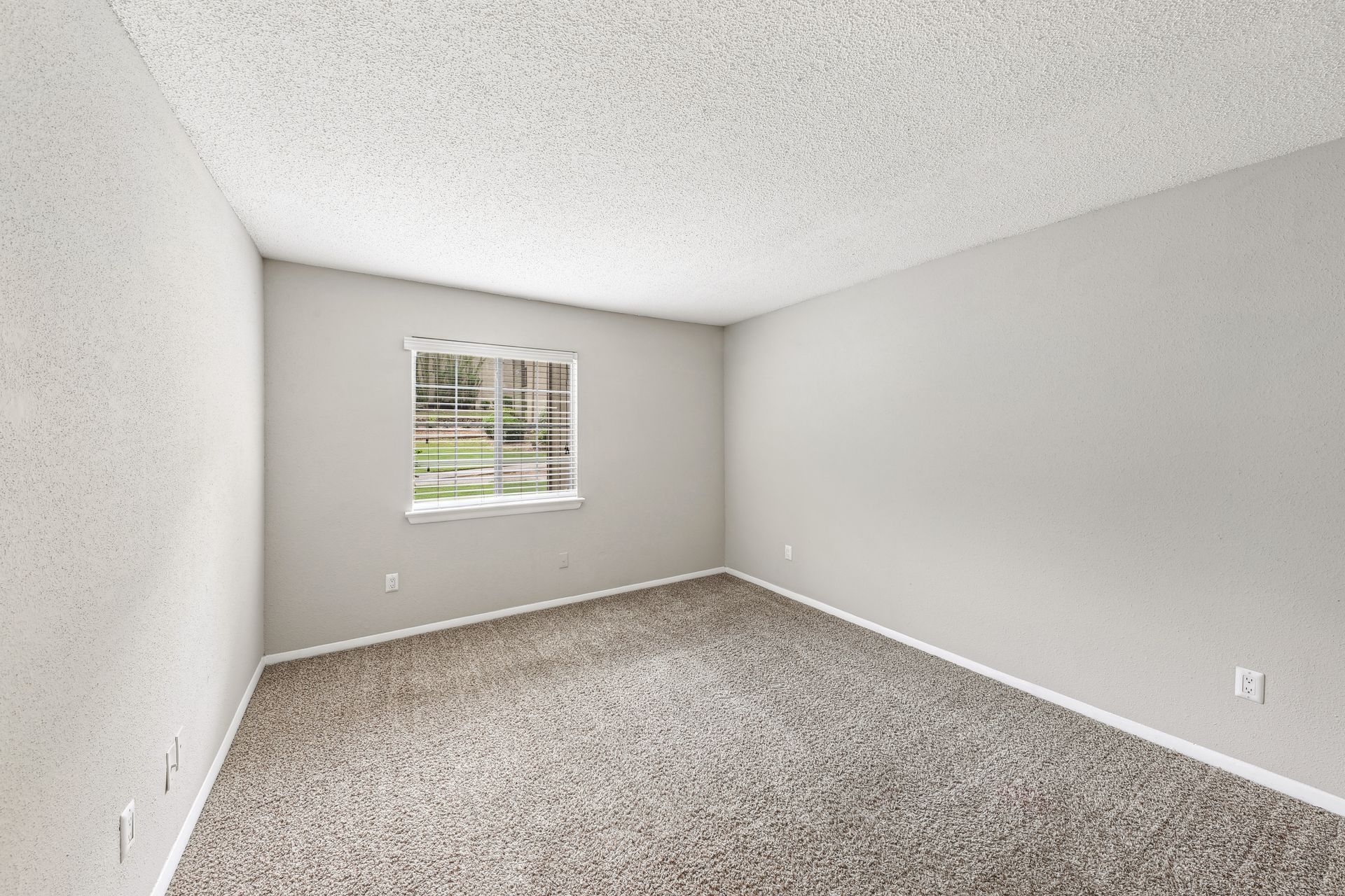An empty bedroom with a window and carpet.