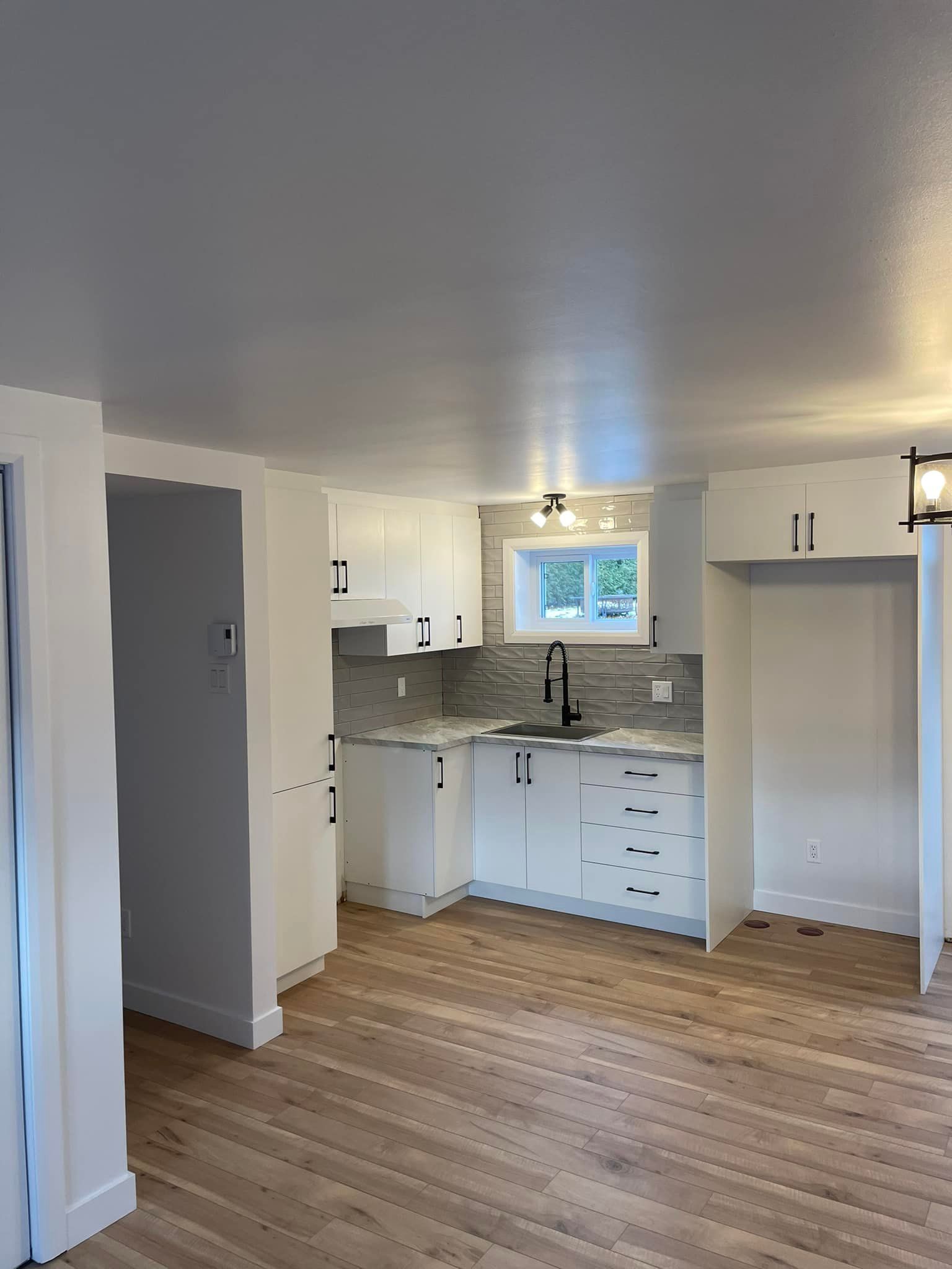 Une cuisine vide avec des armoires blanches et du parquet