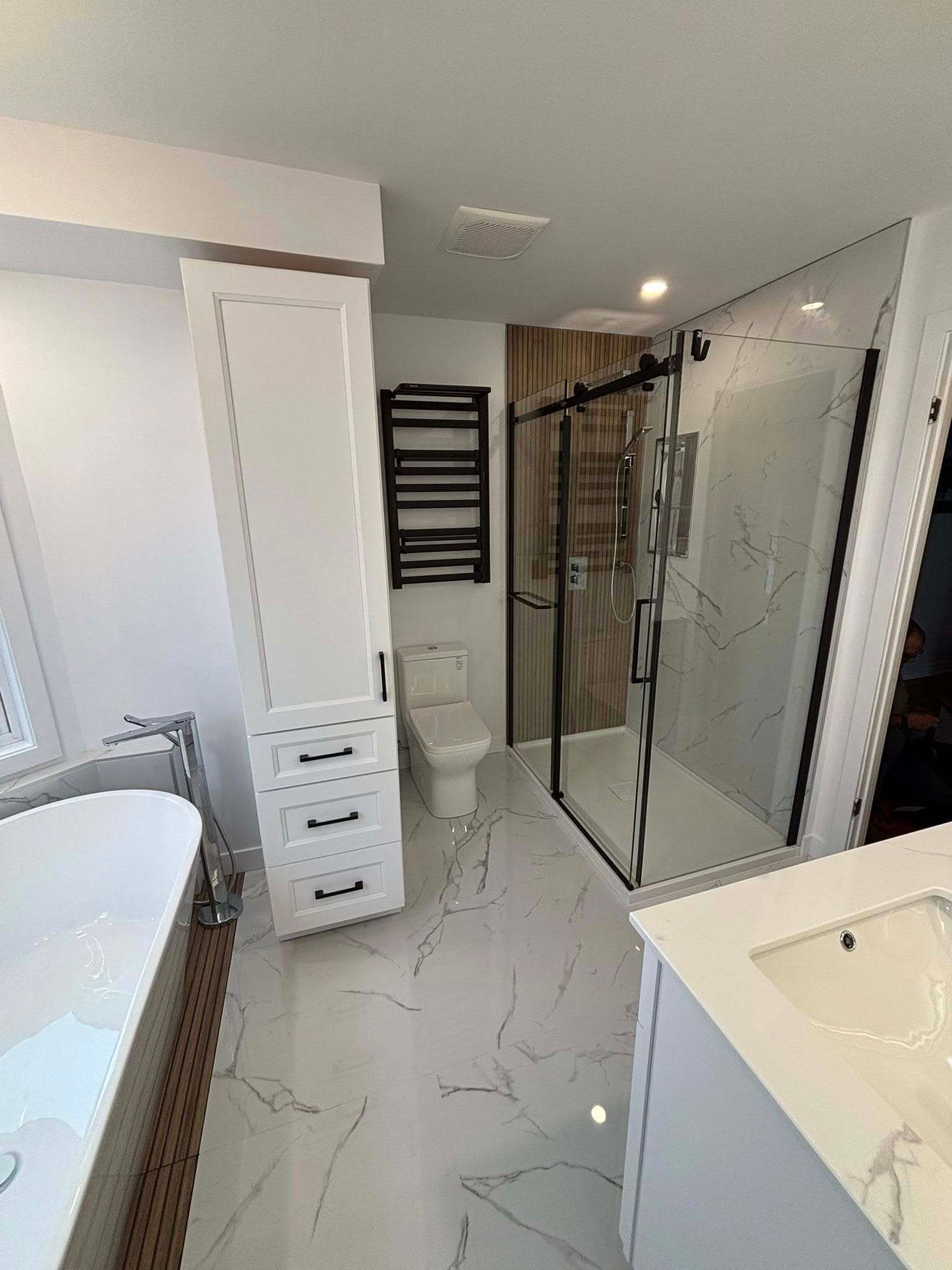 Salle de bains moderne avec meuble-lavabo blanc, armoire haute et douche à porte vitrée.